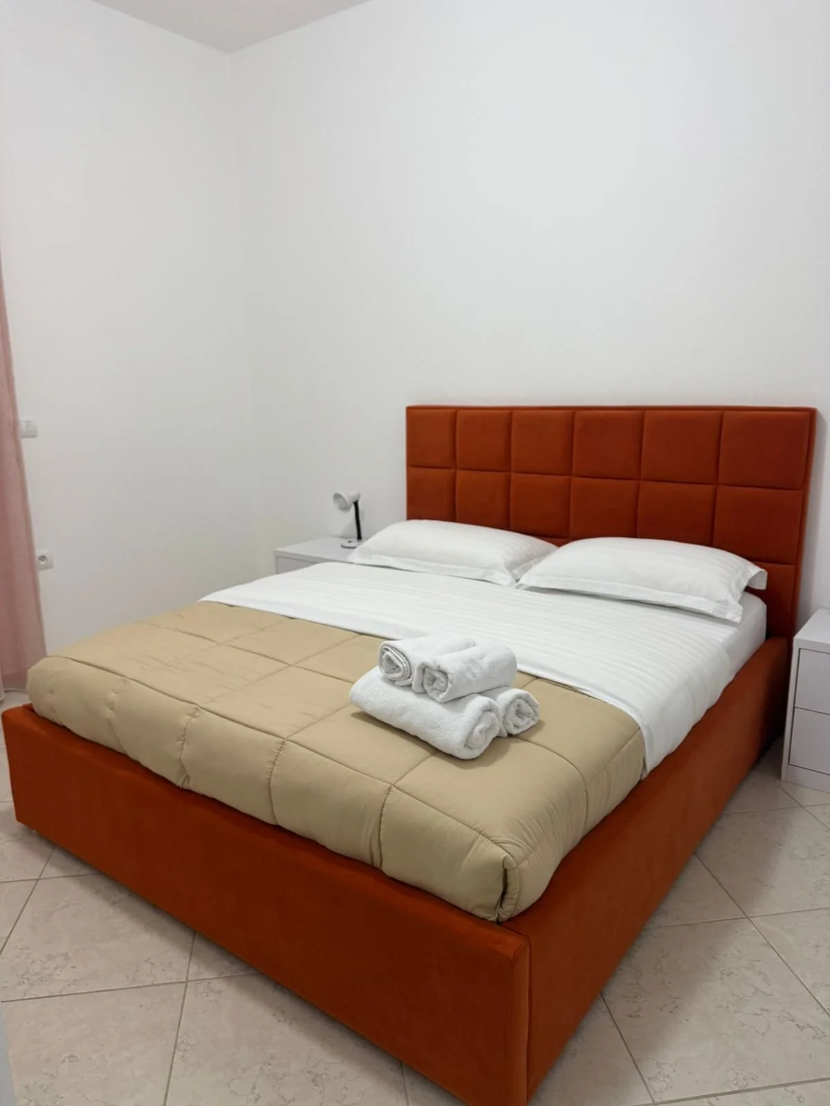 Letto in una stanza con testiera in pelle arancione, coperte beige e asciugamani arrotolati sul letto.