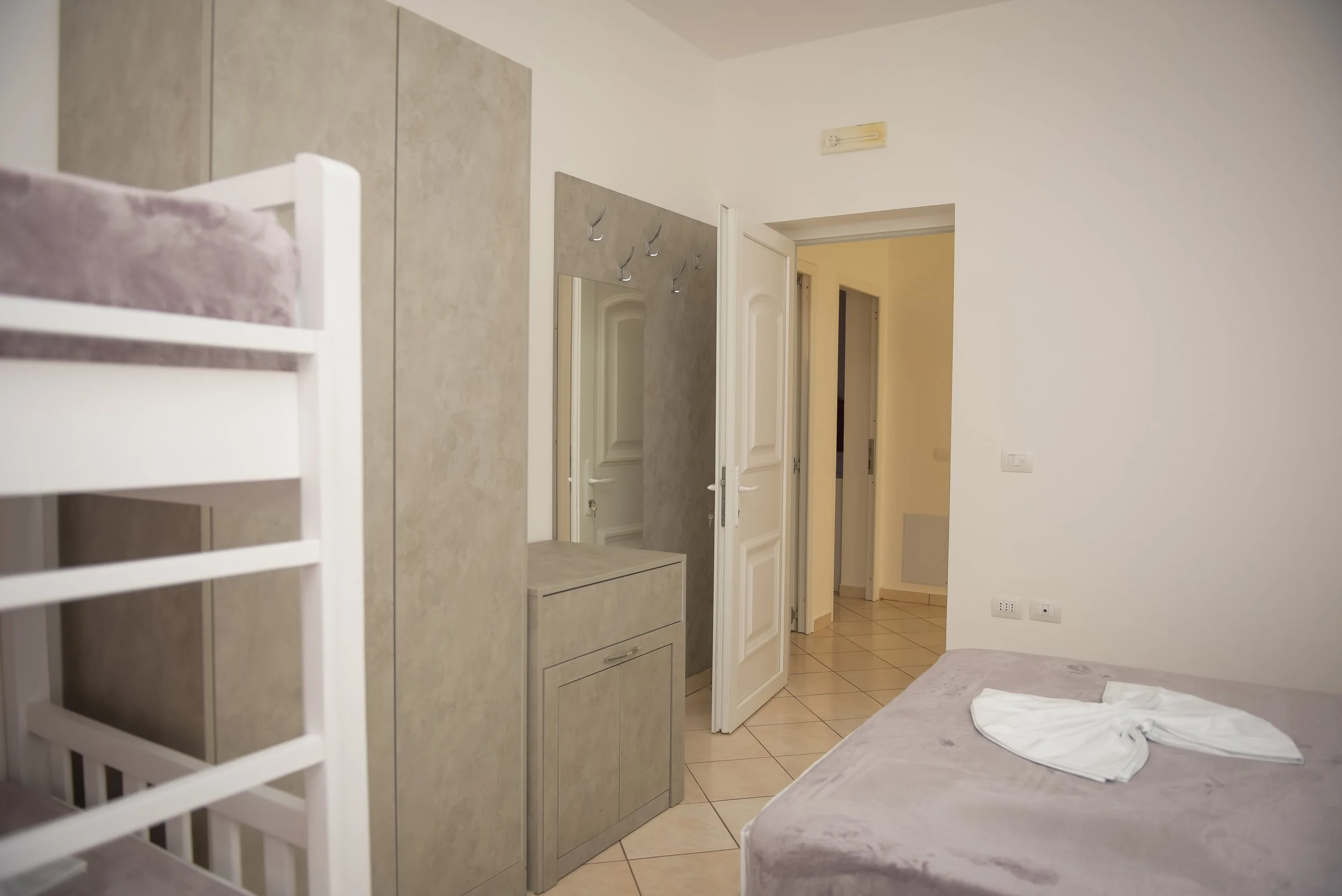 Camera da letto con letto, armadio, pareti bianche, pavimento in piastrelle e porta aperta che conduce ad un corridoio.