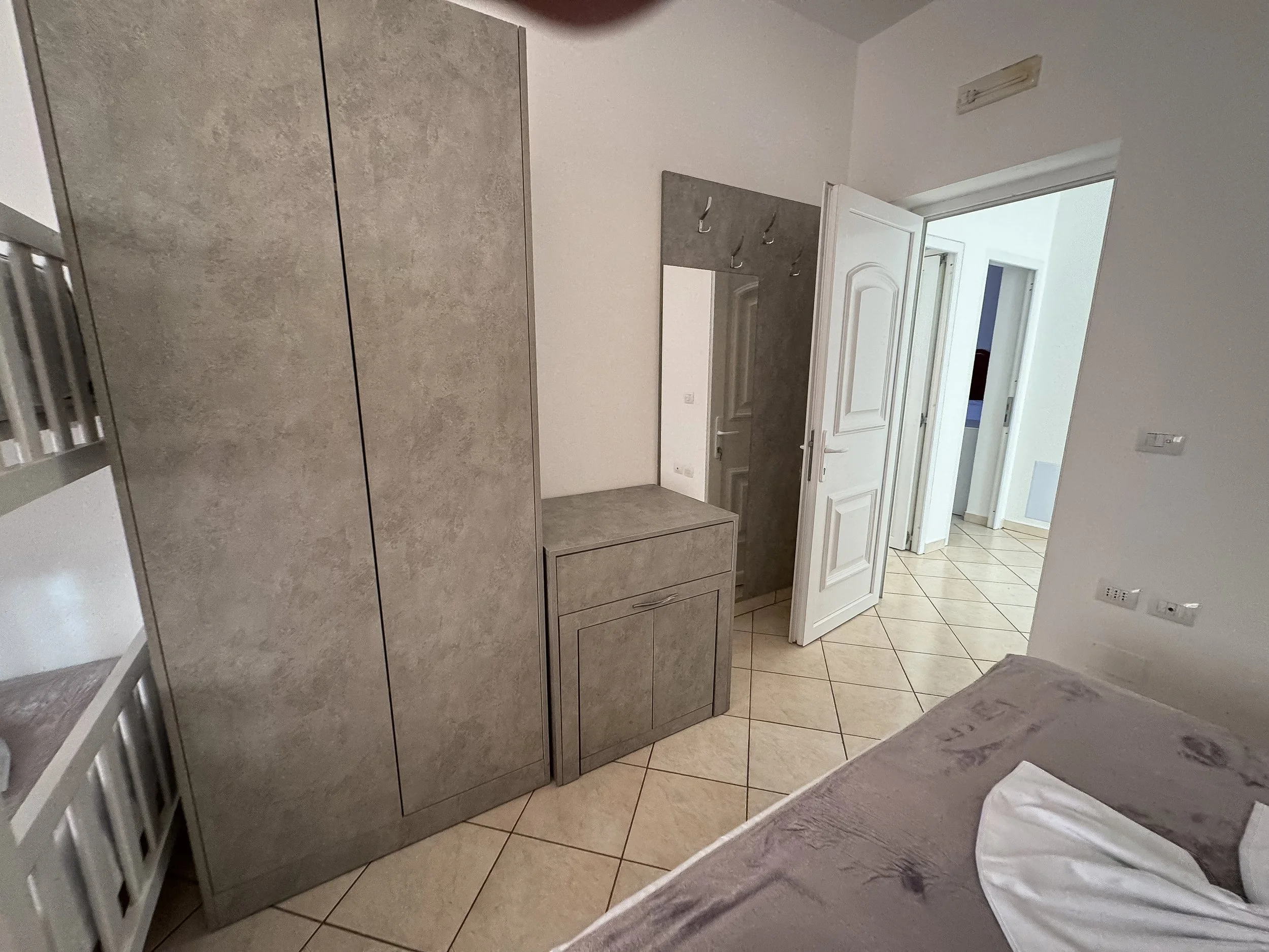 Ingresso con armadio e porta aperta, vista su corridoio e altre stanze, pavimento in piastrelle beige.