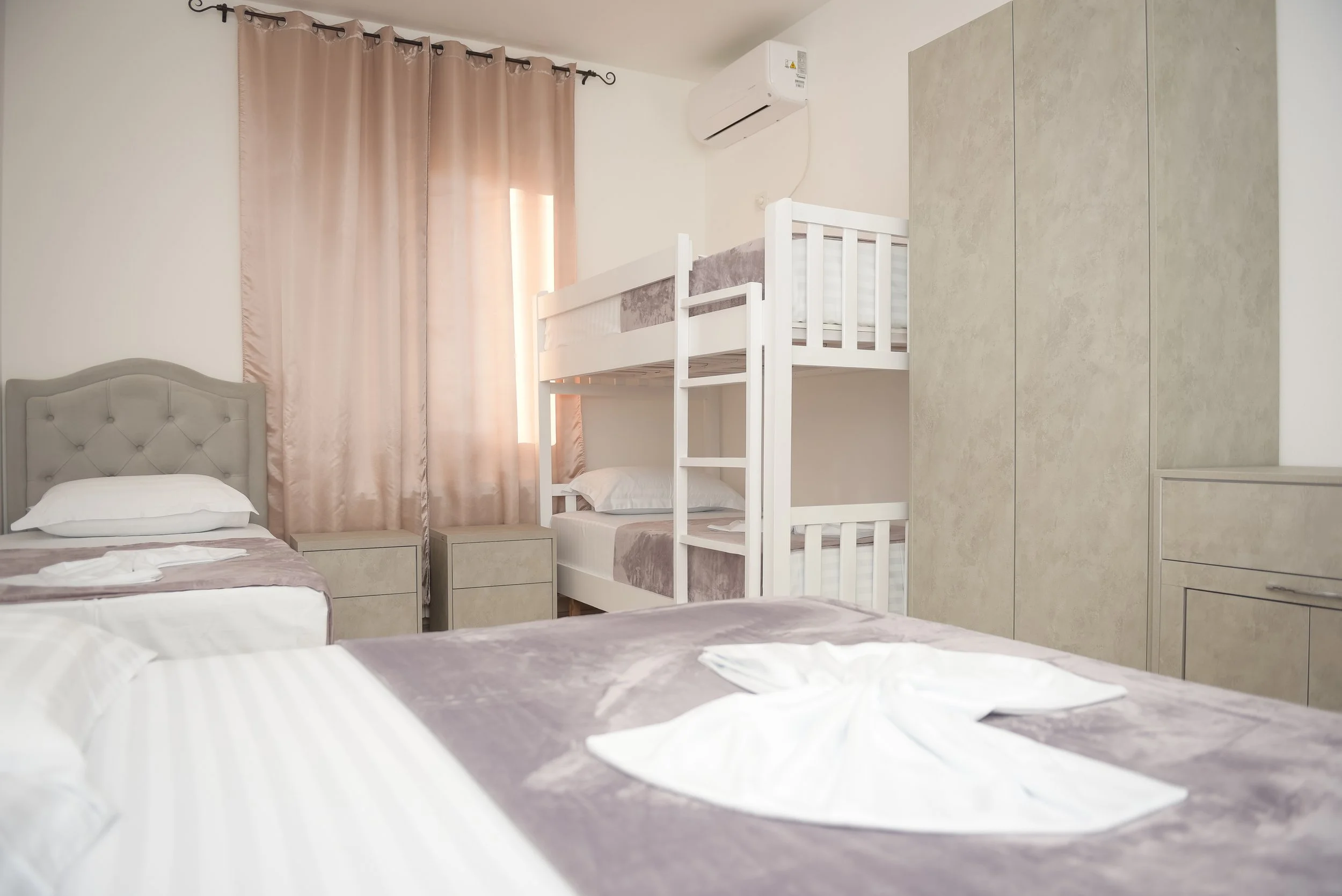 Camera da letto con due letti, una libreria con letto a castello, armadio grande e tende color carne.