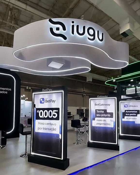 Ambiente de um centro de atendimento ou loja com sinais digitais, incluindo o logotipo da Iugu, e painéis com informações sobre serviços de pagamento, como BetPay, BetGateway e afiliados.