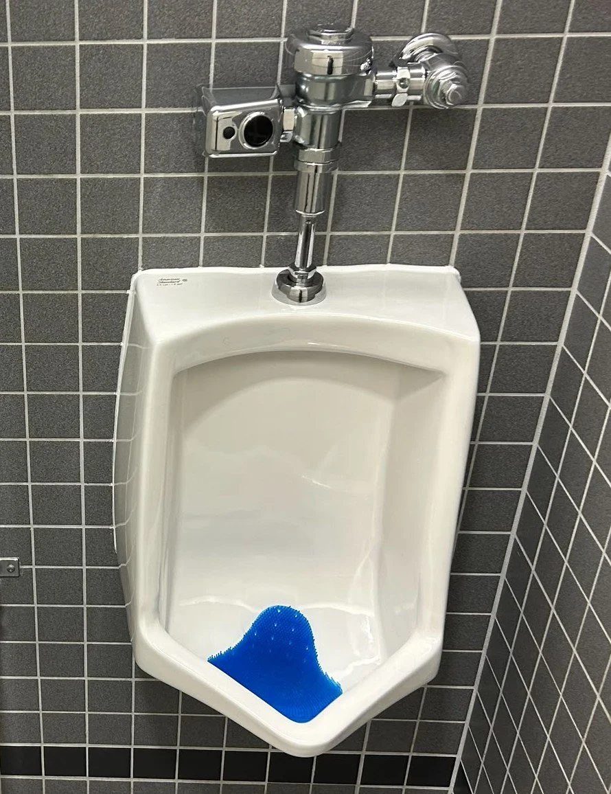 A white urinal with a chrome flush valve mounted on a tiled wall.