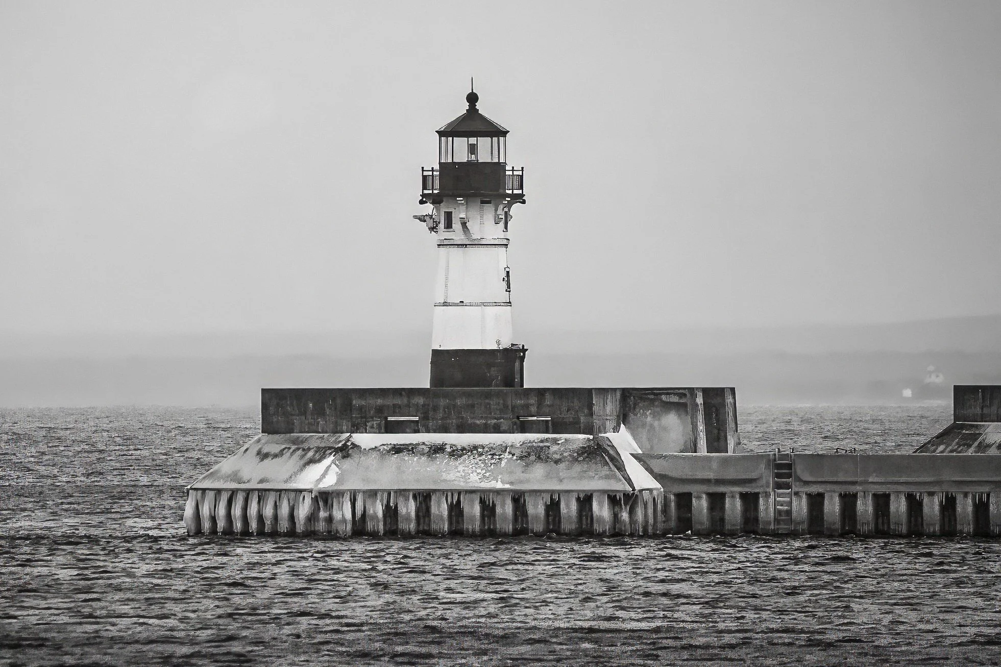 A black and white photo of a lighthouse on a small island, surrounded by water and a stormy sky.