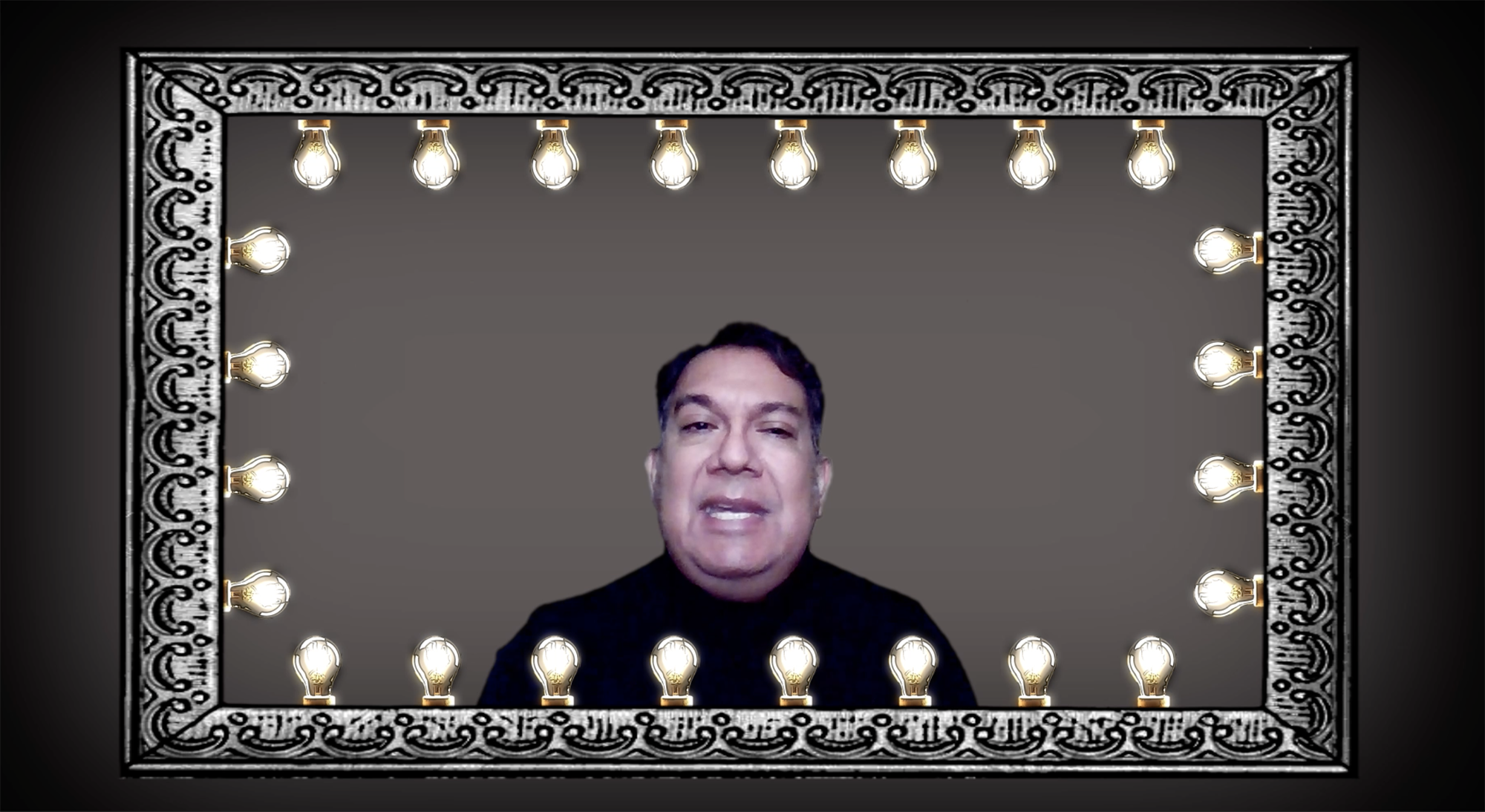 A man with dark hair and a black shirt appears in a frame decorated with light bulbs and ornate silver trim, resembling a dressing room mirror.
