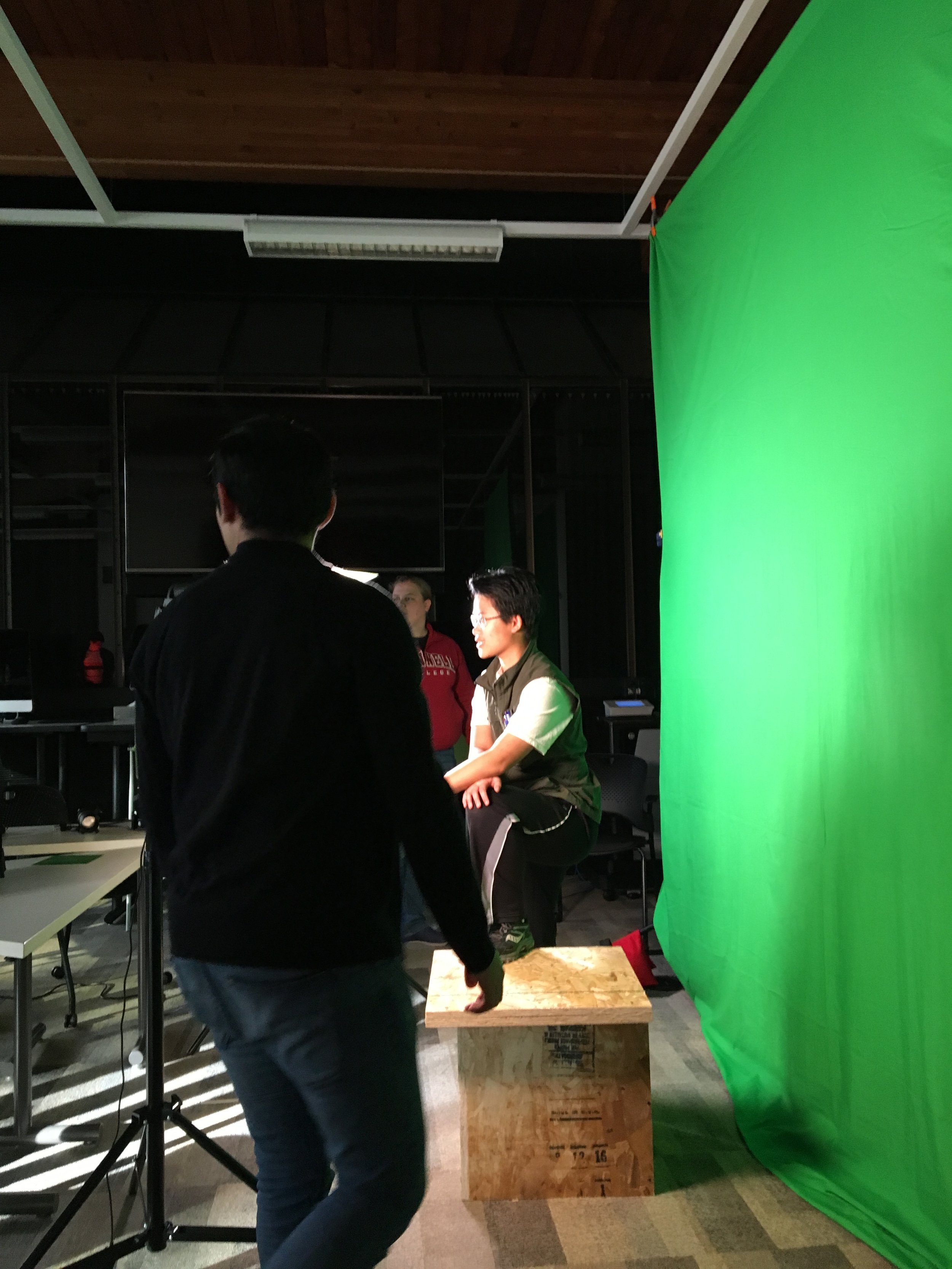 People working in a photo studio with a green screen and a wooden box.