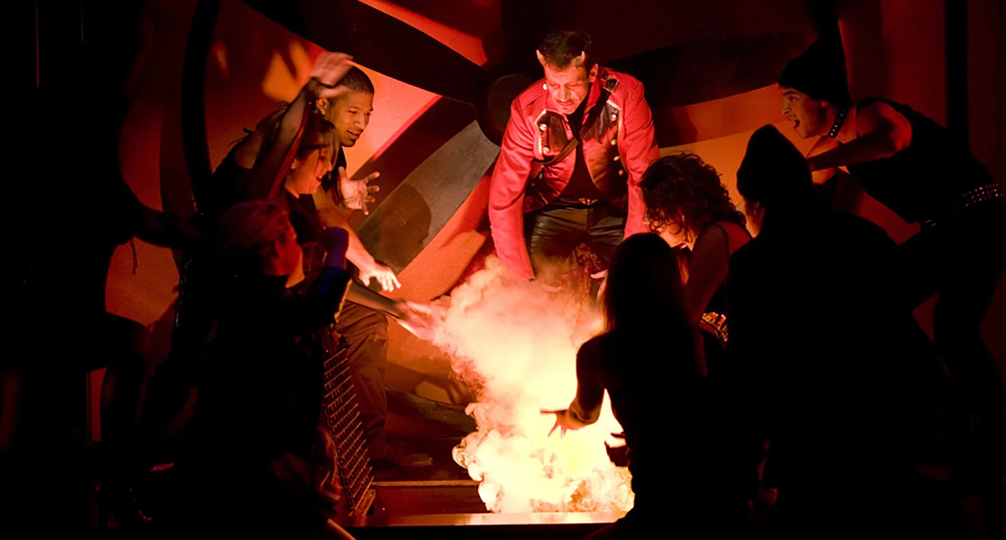 Group of people gathered around a science experiment with fire and smoke, engaging in a dramatic demonstration.