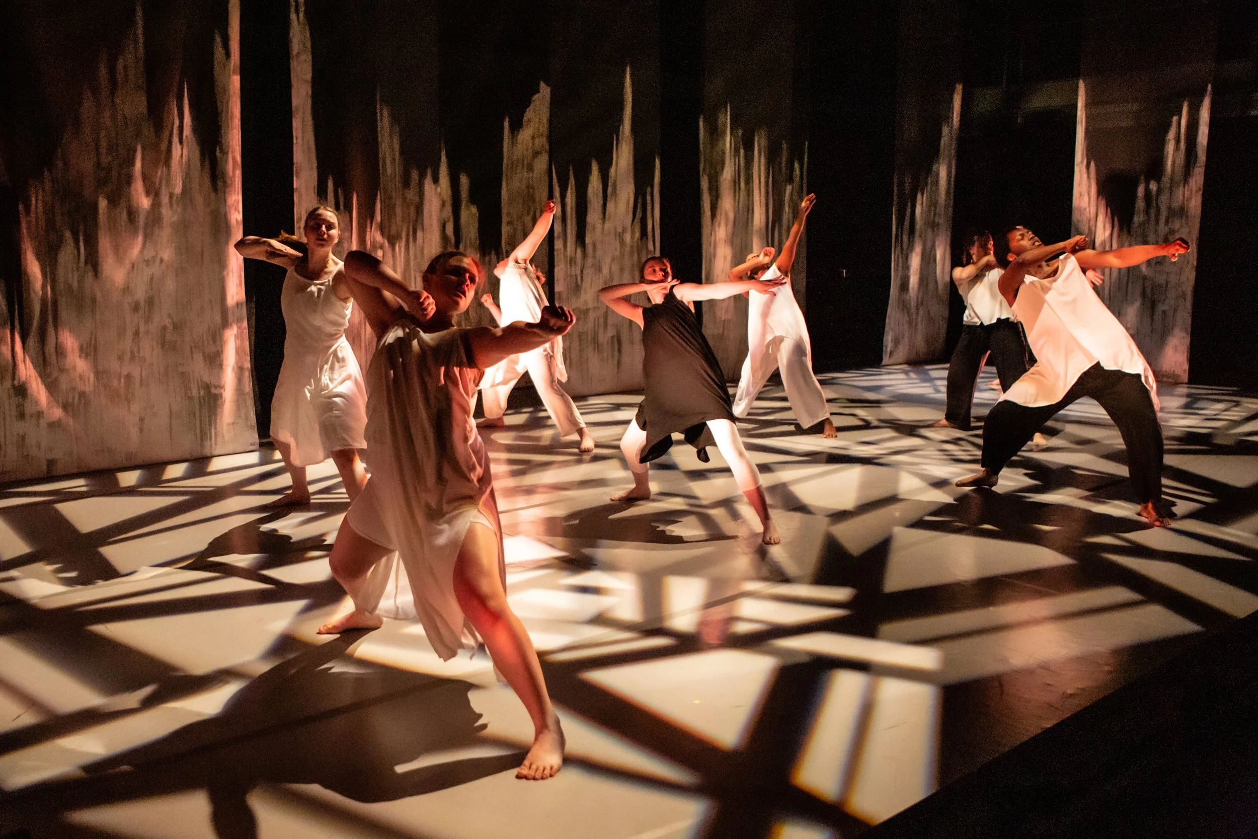Group of dancers performing on stage with dramatic shadow effects on the backdrop.