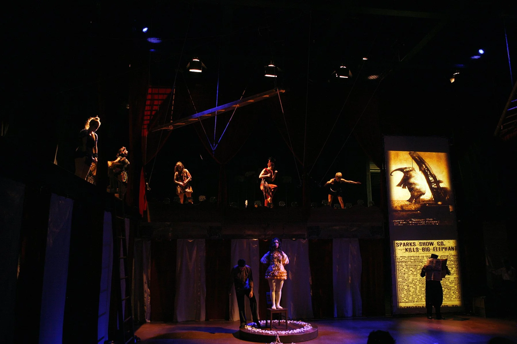 Circus performers on stage, with a vintage-style poster of a big elephant and a worker at a construction site in the background, dark lighting with spotlights highlighting the performers.