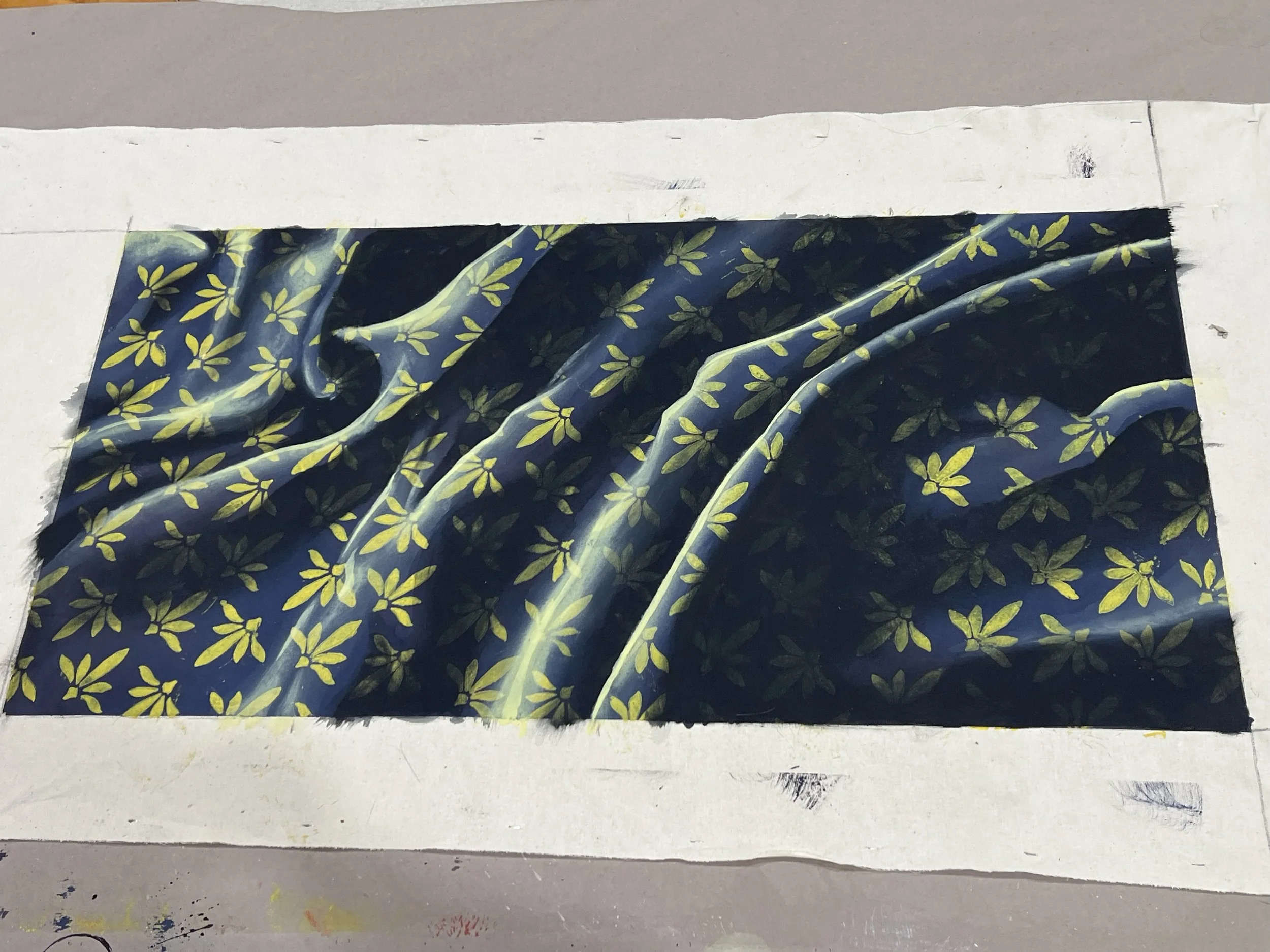 Close-up of folded dark fabric with yellow floral pattern resting on a white surface, with a white strip at the top and visible creases.