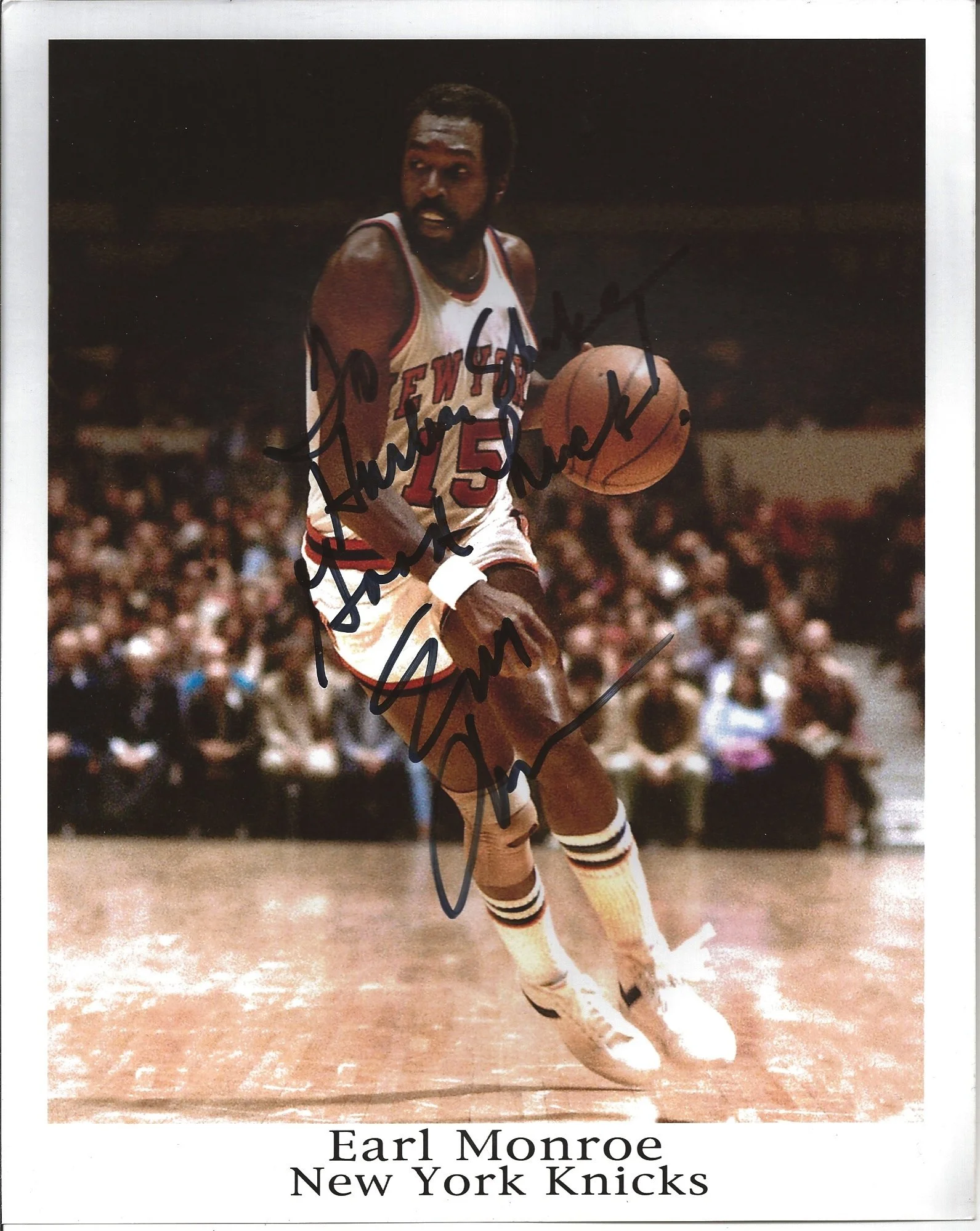 Autographed black and white photograph of Earl Monroe in a New York Knicks uniform, dribbling a basketball on court, with a crowd in the background. The autograph is written across the photo.
