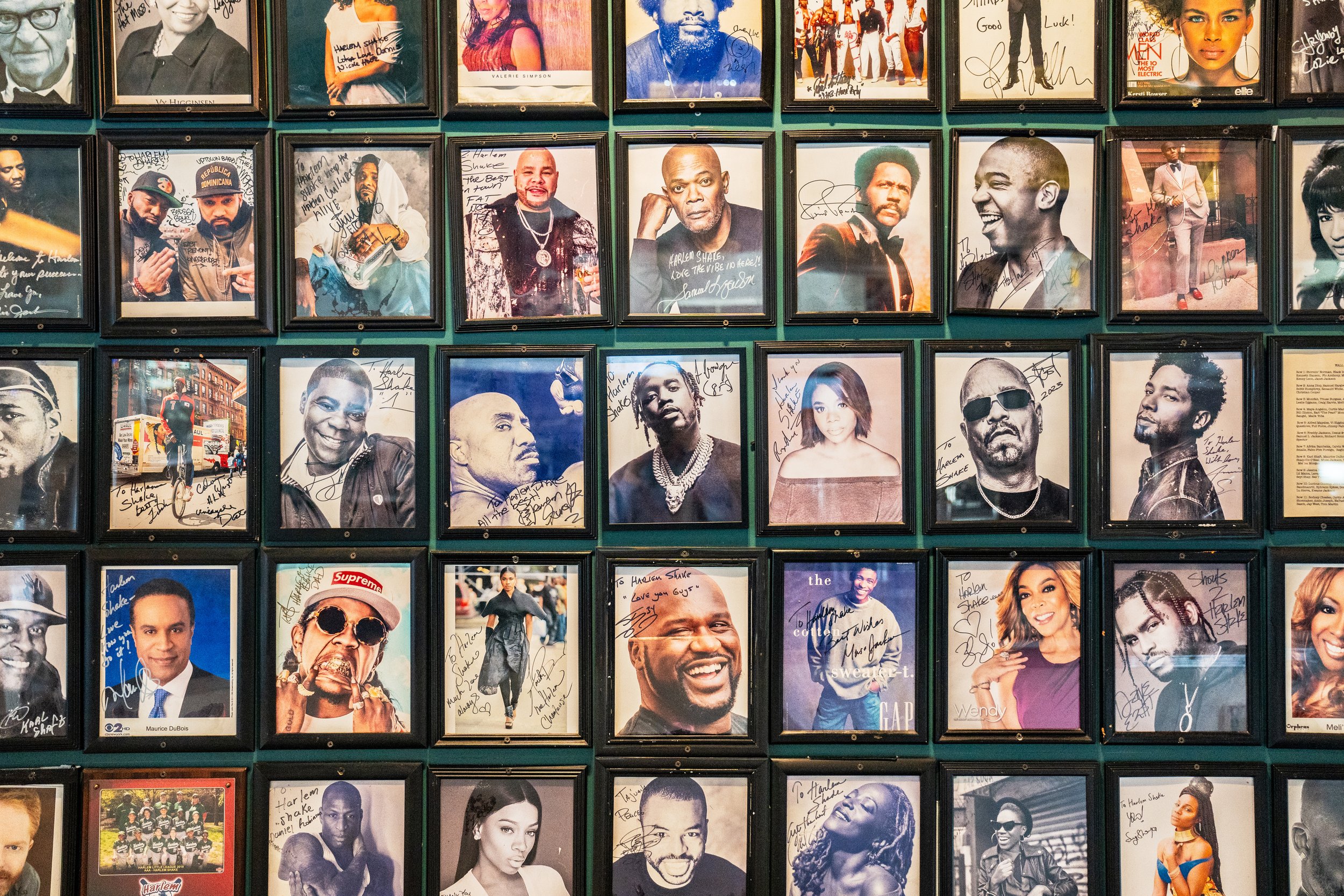 A wall decorated with framed autographed photographs of various celebrities and notable figures in a grid pattern.