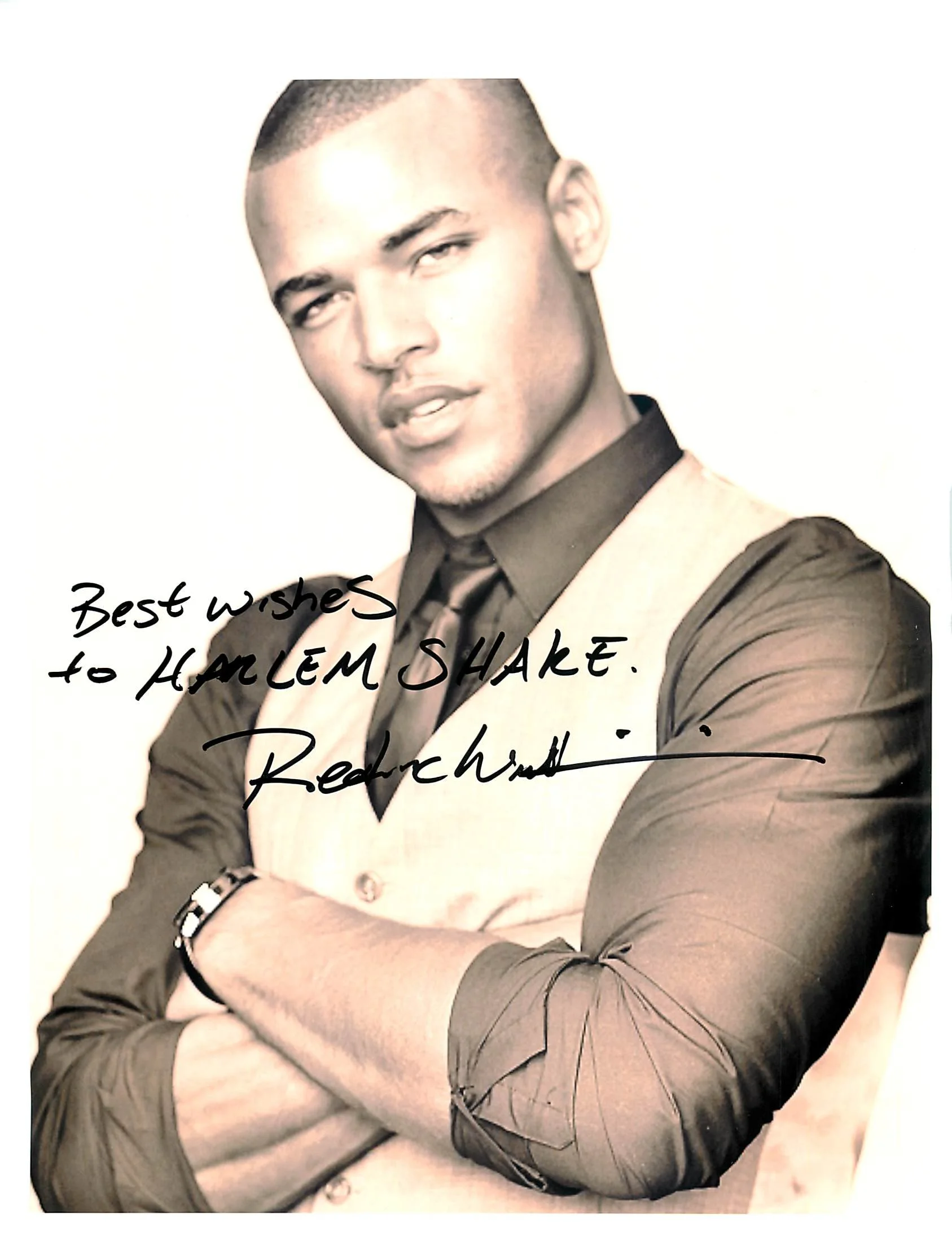 Black and white photo of a young man with short hair, wearing a black shirt and a white vest, crossed arms, with handwritten text that says "Best wishes to Harlem Shake".