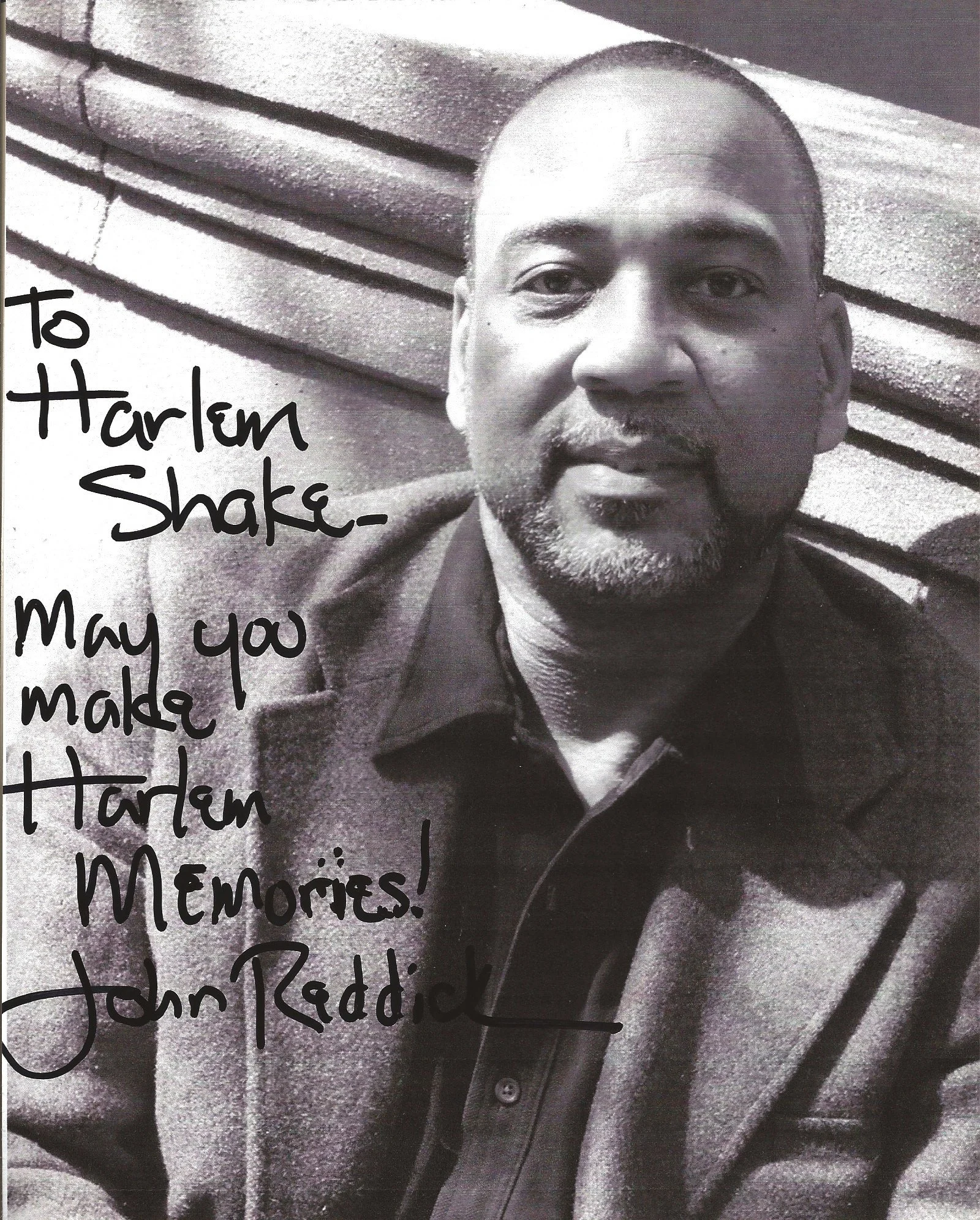 Black and white photo of a man with short hair and a beard, smiling slightly, wearing a jacket over a shirt, sitting against a textured wall with horizontal lines. handwritten text on the image reads: 'to Harlen Shake- May you make the biggest memori