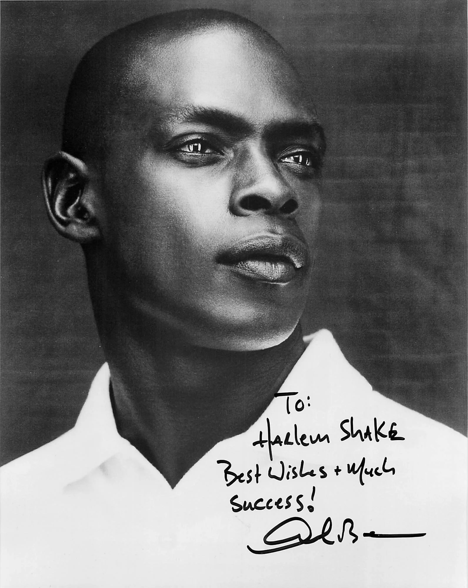 A black and white close-up portrait of a person's face with a serious expression, smooth scalp, and dark clothing, accompanied by a handwritten message on the lower right side that reads: "To: ... Harlem Shake ... Best Wishes & Much Success!".