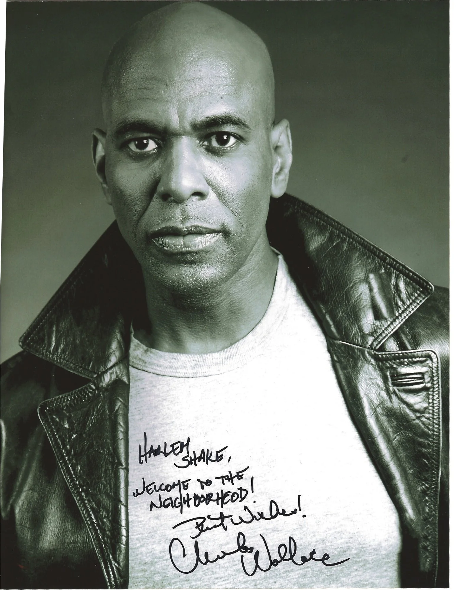 A black-and-white portrait of a man with a shaved head wearing a leather jacket and a light-colored T-shirt with handwritten text, and a handwritten note on a piece of paper.