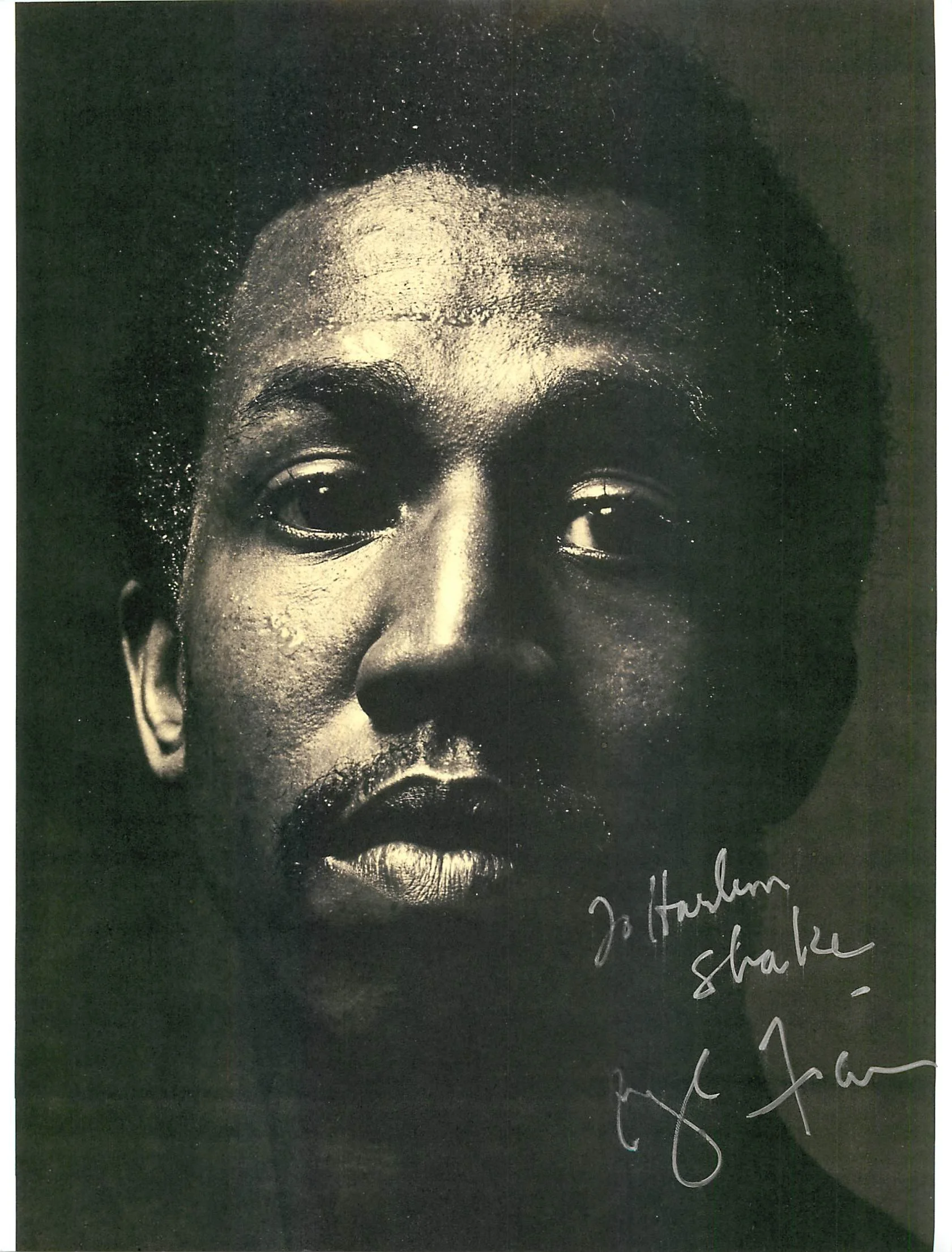 Close-up of a black and white photograph of a person's face, showing their eyes, nose, and the top of their forehead. There is white handwritten text at the bottom right corner of the photograph.