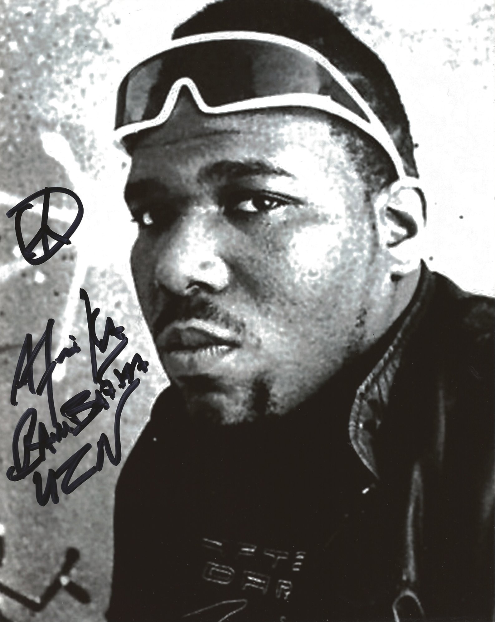 Black and white photo of a young person's face with dark skin, short hair, wearing sunglasses, and a jacket with a collar. There is handwritten text and a peace sign drawn on the photo.