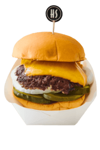 A burger with a sesame seed bun, pickles, onions, a beef patty, melted cheese, and a cup holding a flag with the letters 'HS'.