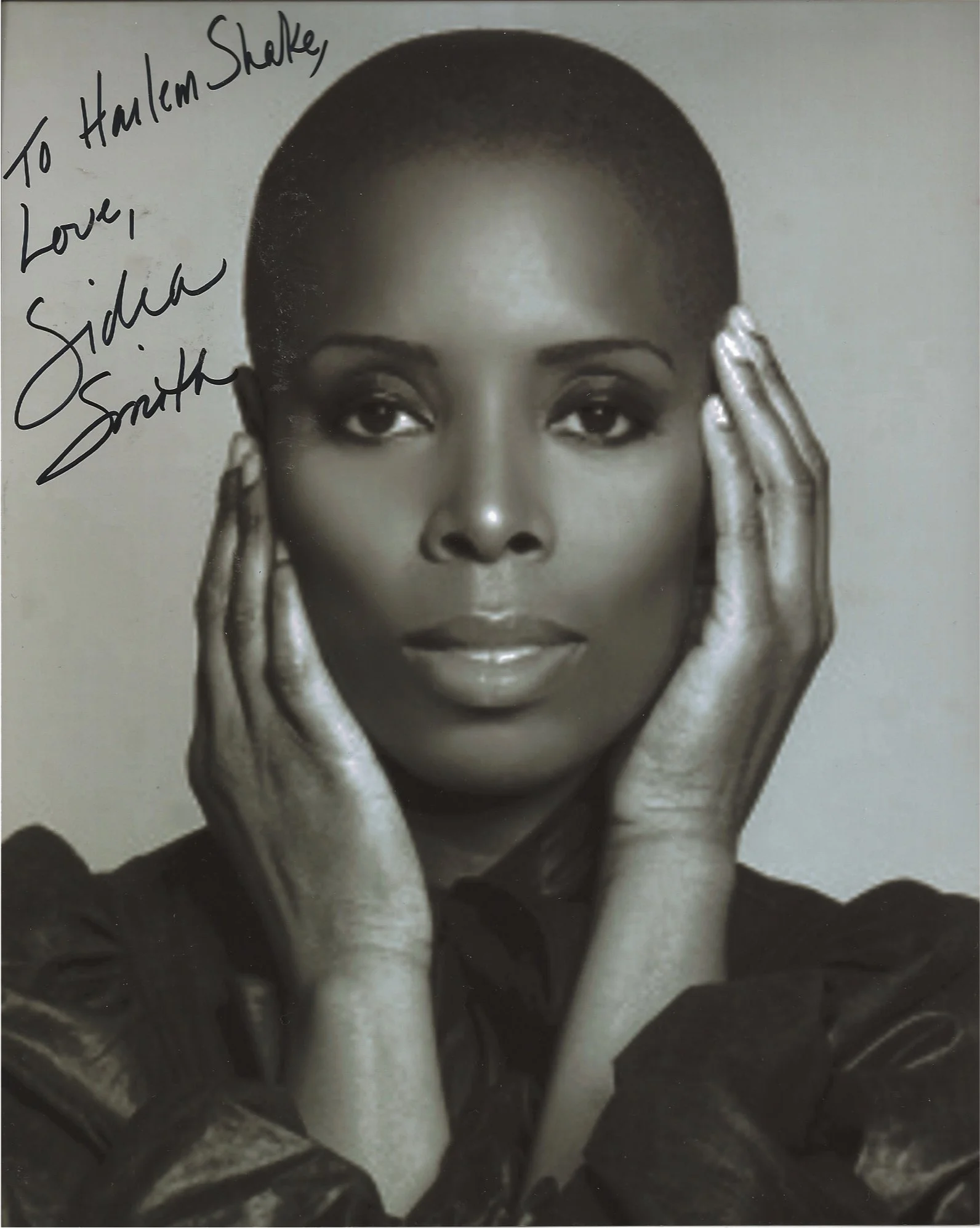 Black and white portrait of a woman with short hair, touching her face with both hands, looking directly at the camera.