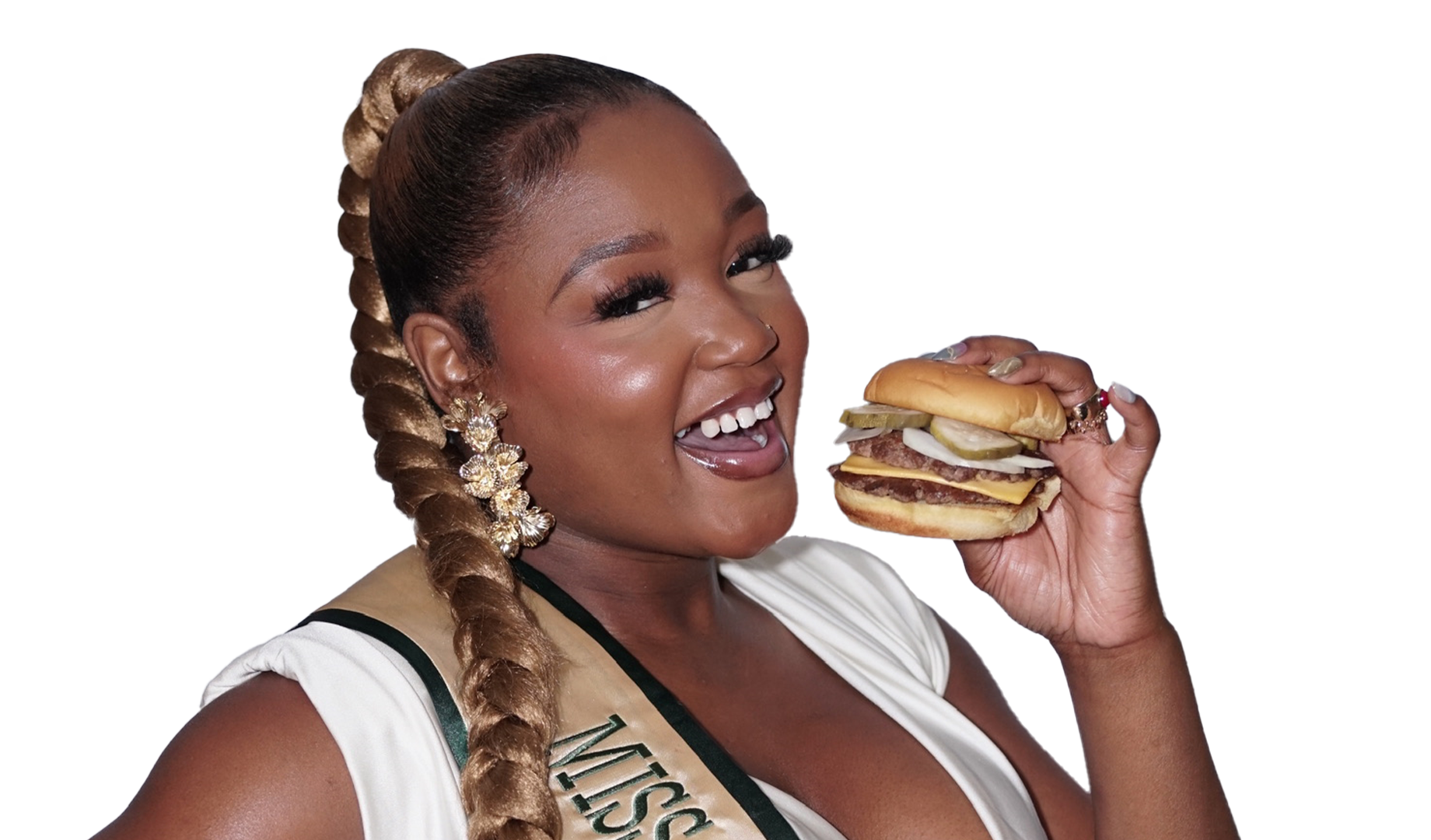 A woman with long braided hair, wearing earrings and a sash, smiling and holding a large cheeseburger with pickles, onions, and multiple beef patties.
