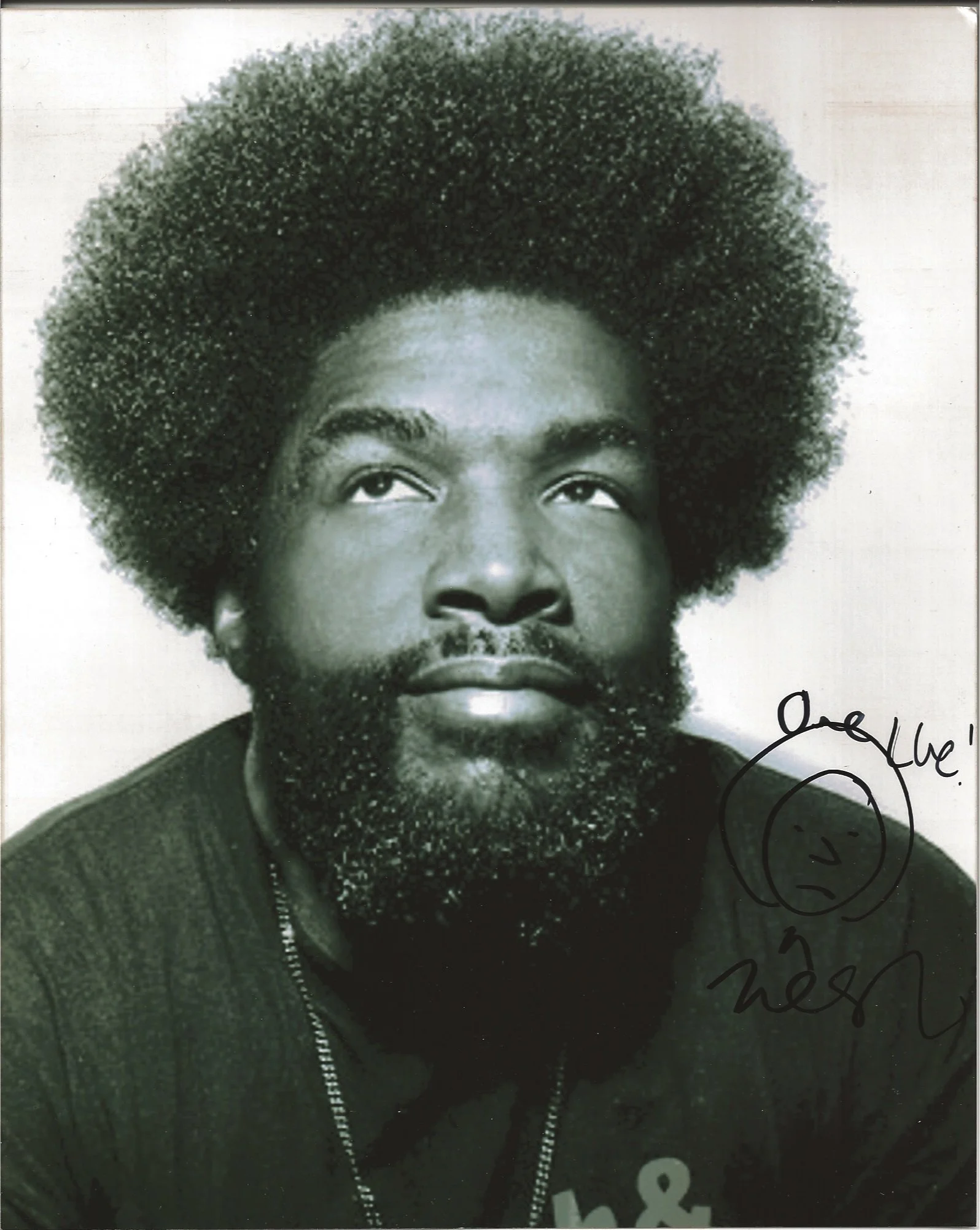 A black and white portrait of a man with a large afro hairstyle and a full beard, wearing a hoodie and looking upward.