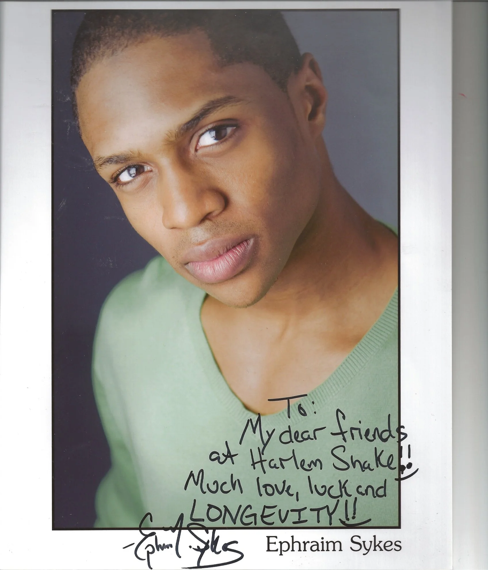 Close-up of a young man with a serious expression, looking at the camera, with dark skin, short dark hair, and wearing a green shirt. Overlayed on the bottom right corner are handwritten notes and signatures, including the message: 'To: My dear frien