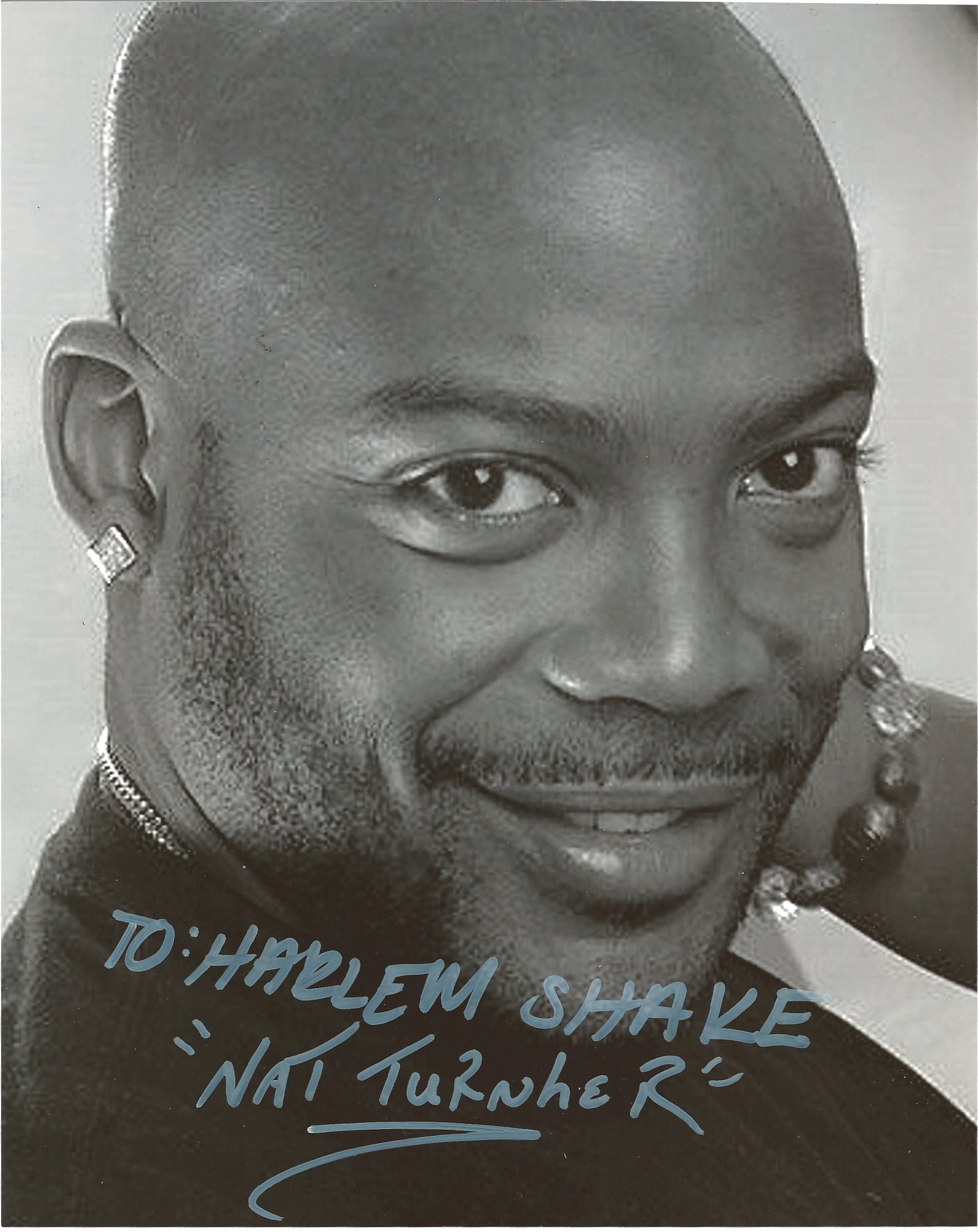 Close-up black and white photo of a smiling woman with short hair and earrings, wearing a top with text and decorative elements.