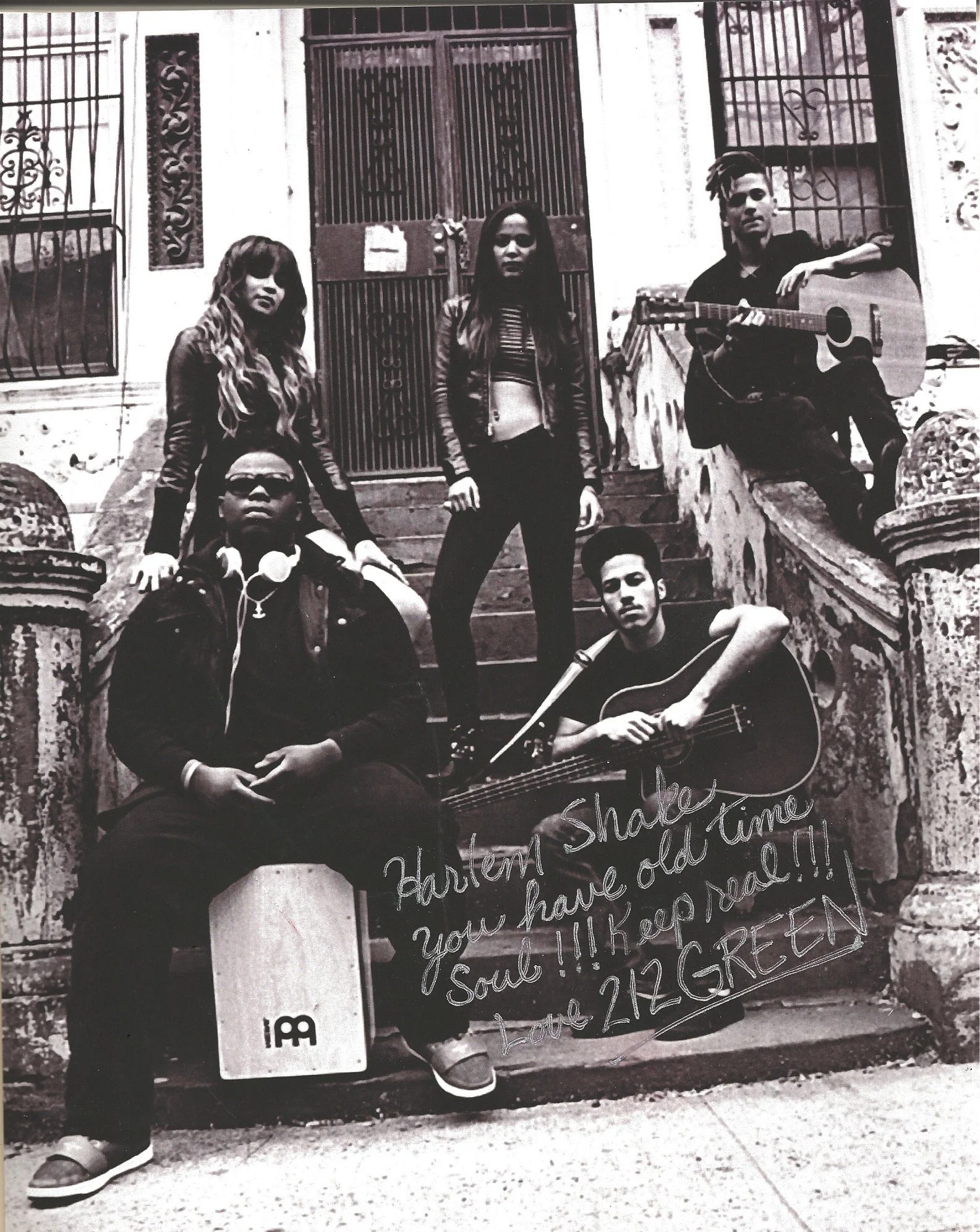 A group of five young people posing on the steps of a building with ornate architectural details, one person holding a guitar, and a handwritten sign with messages about keeping the soul and respecting the elders.
