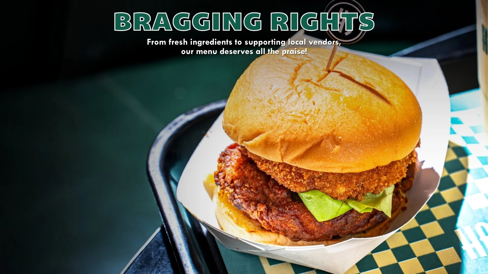 Close-up of a fried chicken sandwich with lettuce on a bun, served on a tray with a checkered paper liner.