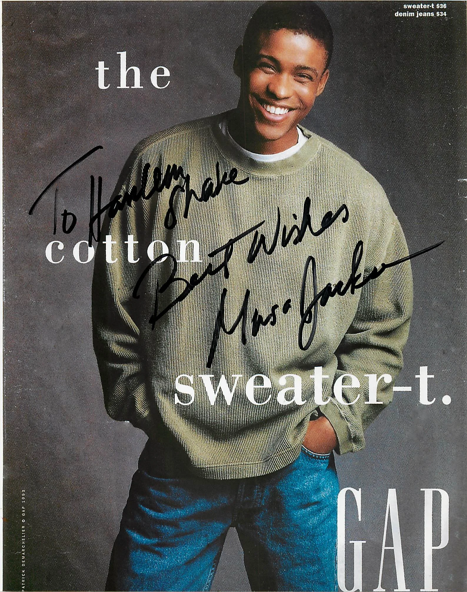 A young man wearing a green sweatshirt and jeans, smiling with his hands in his pockets, against a dark background.