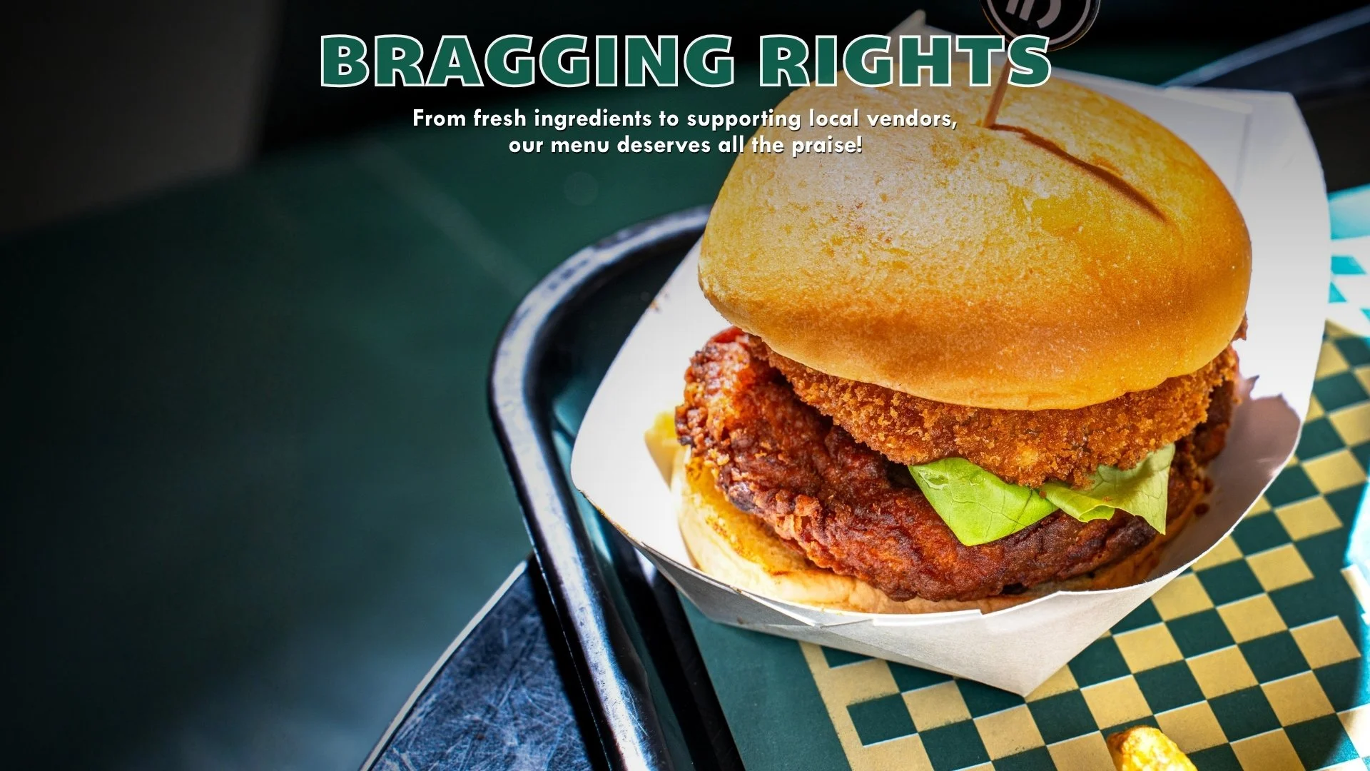 Close-up of a fried chicken sandwich with lettuce on a bun, served on a tray with a checkered paper liner.