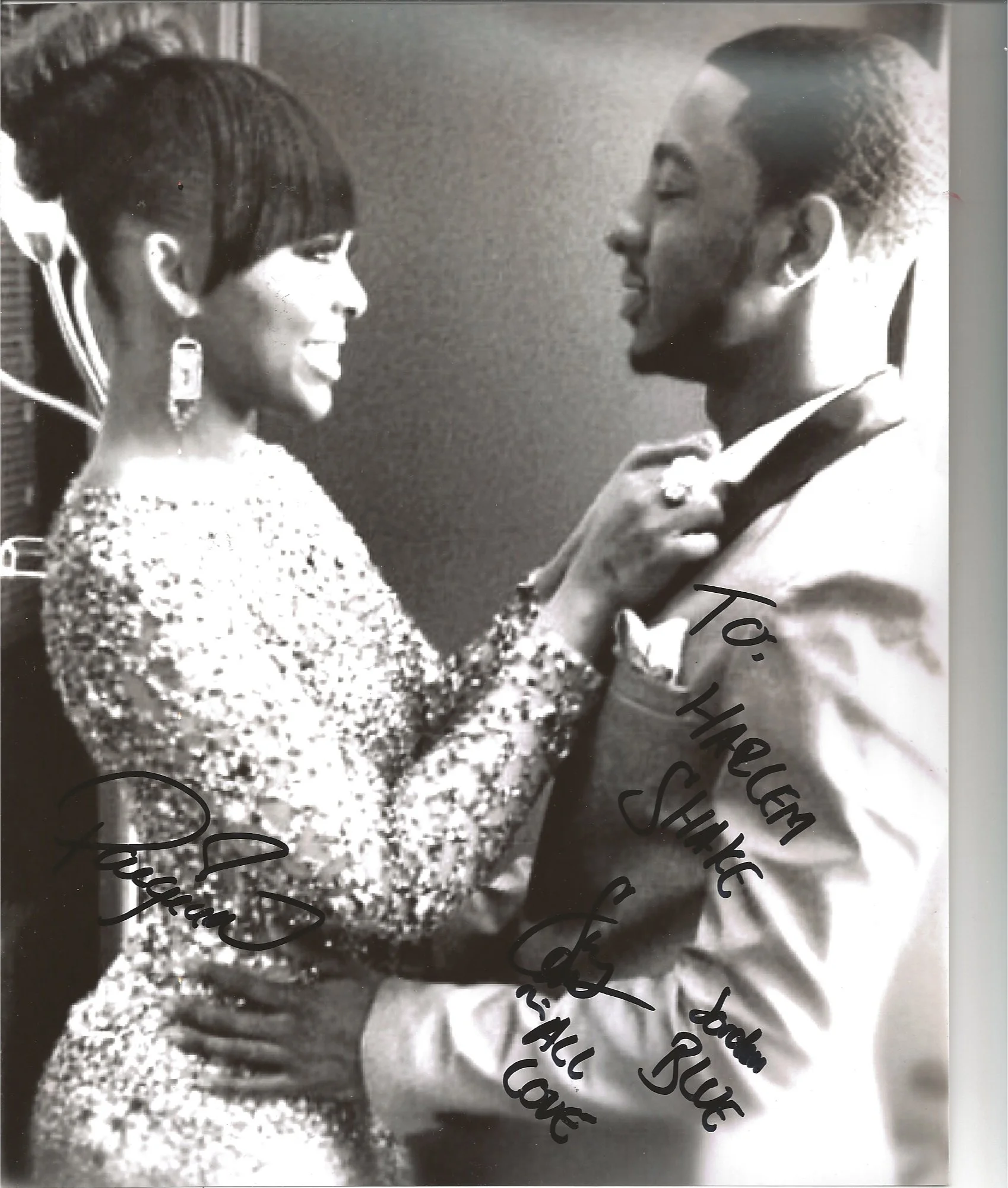 A black-and-white photograph of a smiling woman with styled hair and earrings, facing a man in a suit and tie, who is also smiling and holding her shoulder. The woman has her hand on the man's chest. There is handwritten text over the image.