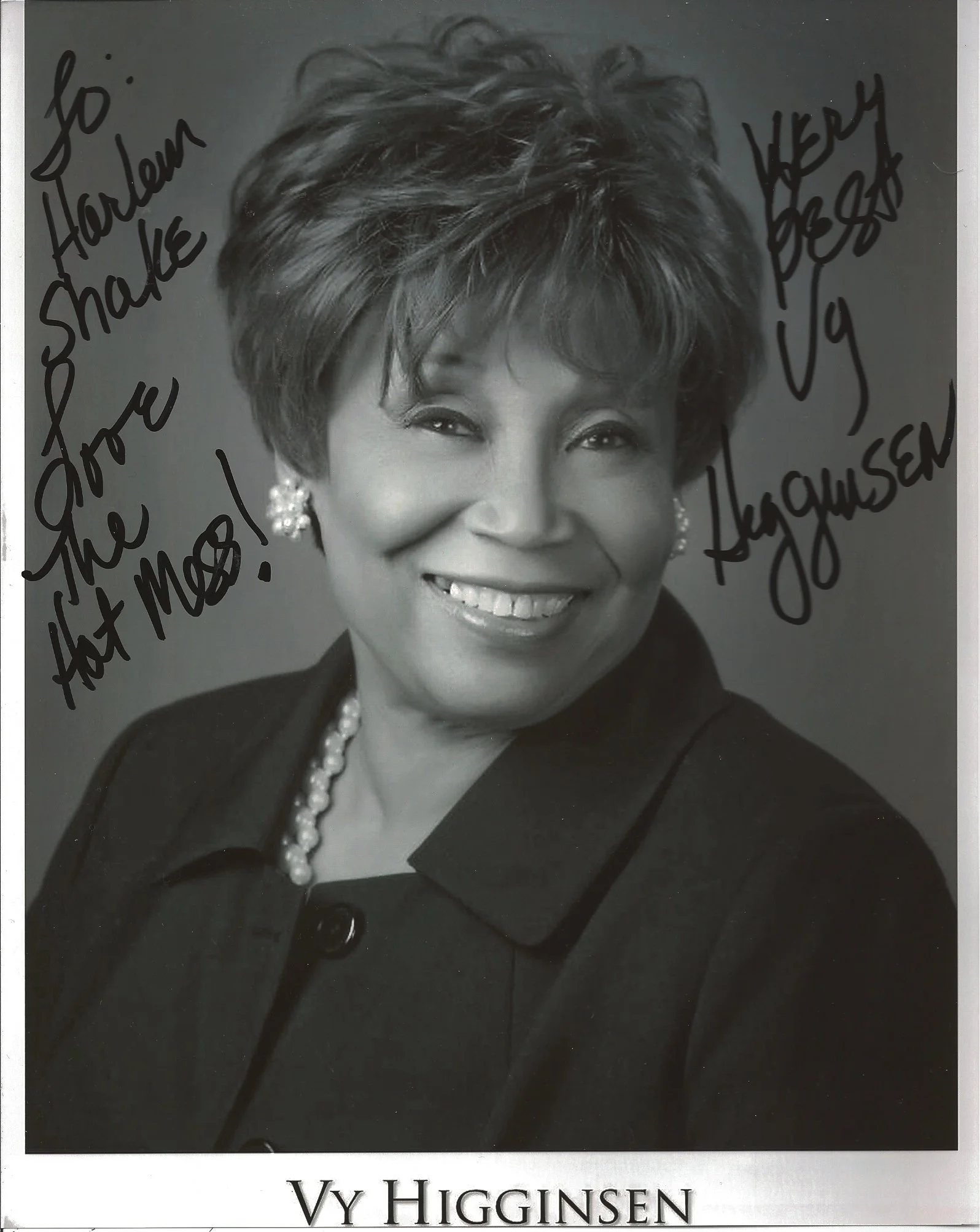 Black and white portrait photograph of Vy Higginsen, smiling girl with short styled hair, wearing earrings, a pearl necklace, and a suit with a lapel pin. Handwritten notes in black ink on the photograph say, 'god Hallowed be your name,' and 'Here Be