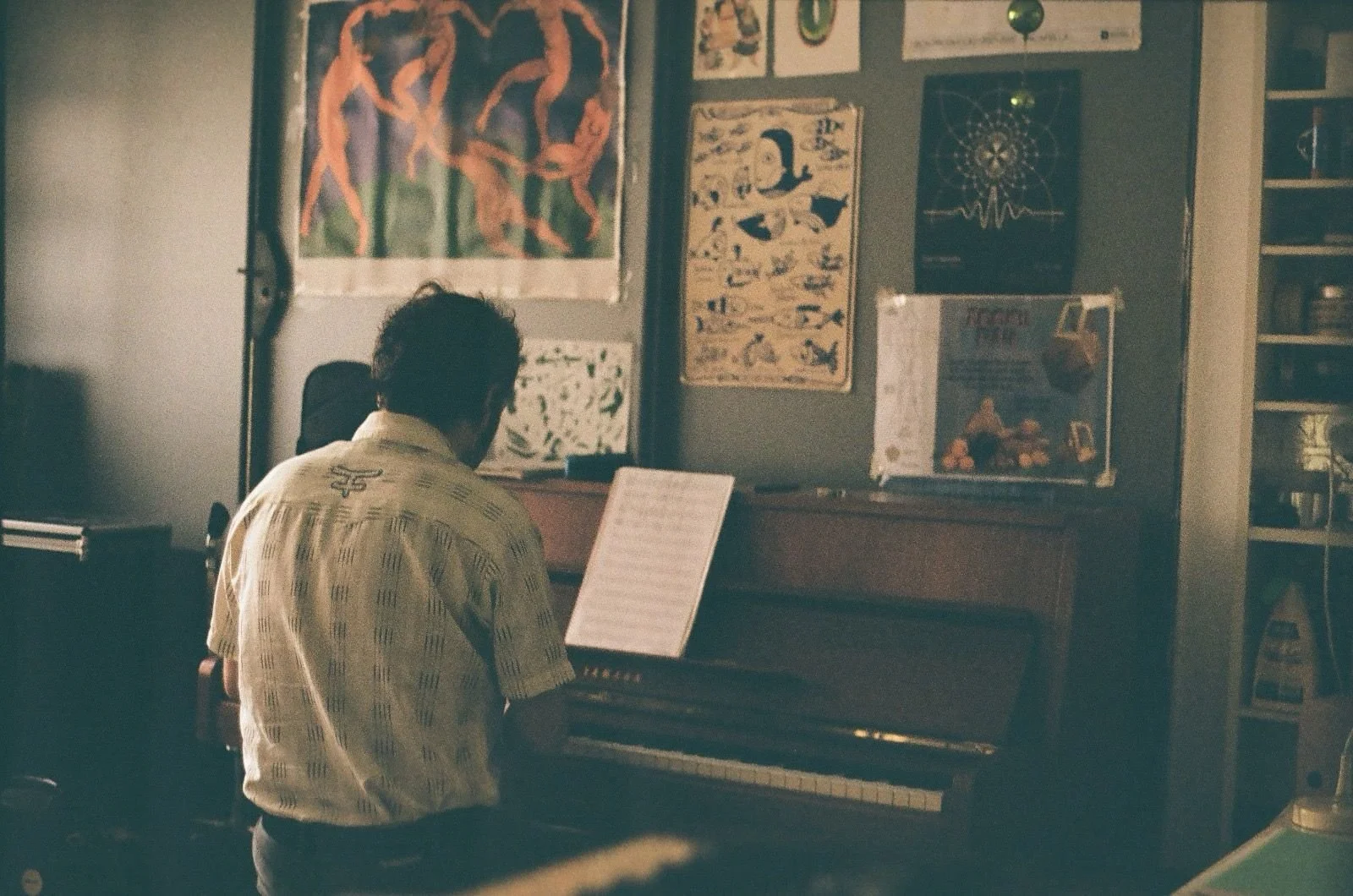 Hombre tocando el piano en una sala decorada con carteles en la pared.