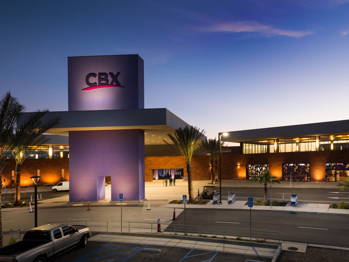 Exterior of the Cross Border Xpress in Otay Mesa, California framed by palm trees and a clear evening sky.