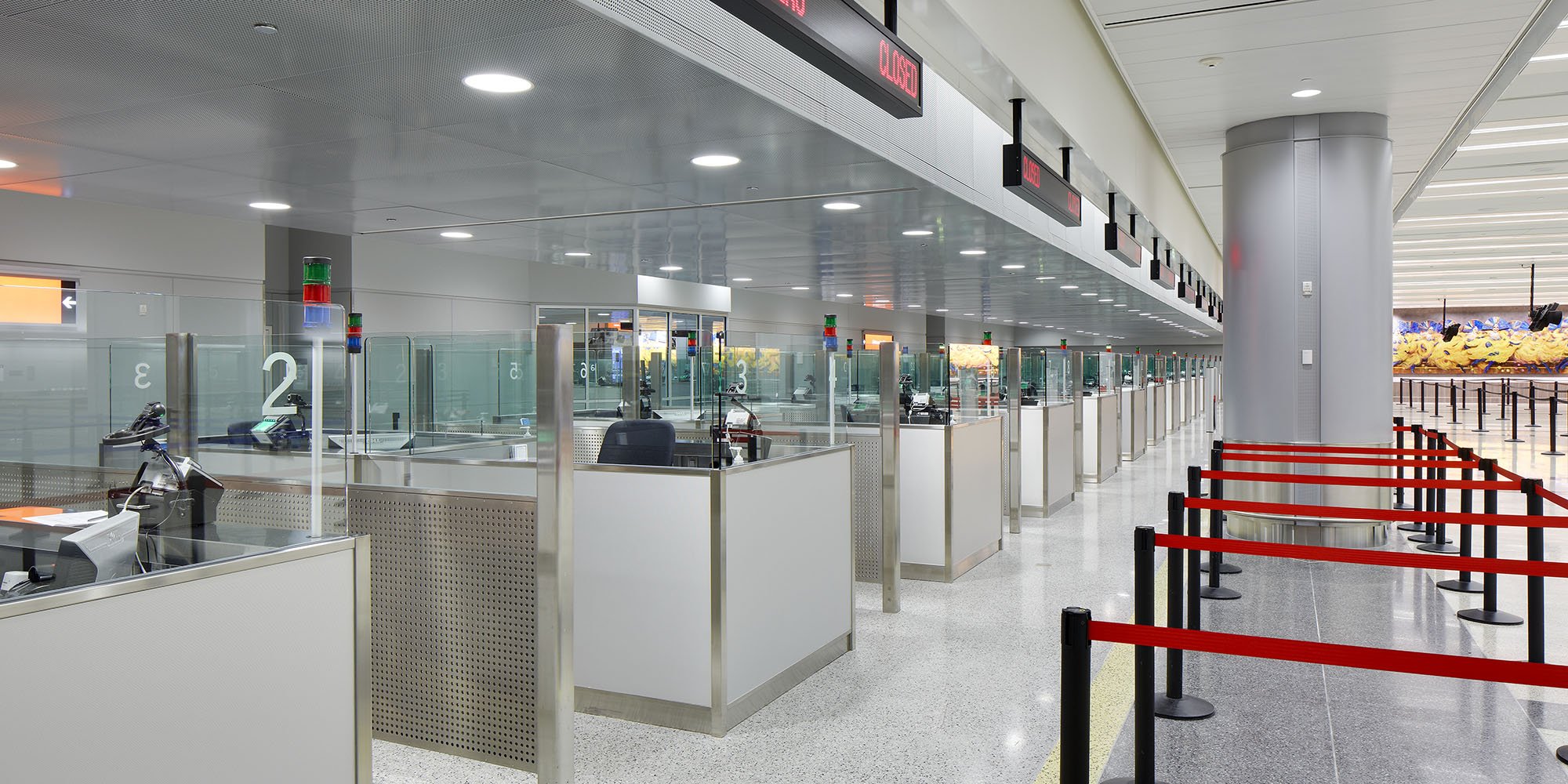 Newly constructed customs inspection booths at Las Vegas International Airport with security barriers, digital screens displaying "Closed", and a colorful mural on the wall in the background.