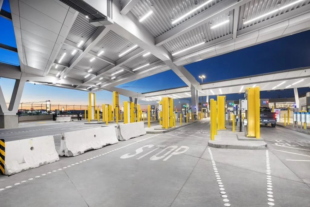 Newly constructed primary inspection lanes at the Calexico West Port of Entry. Yellow protective barriers are positioned under a large modern canopy at dusk, with a dark blue sky in the background. (Photo by Mikki Piper)