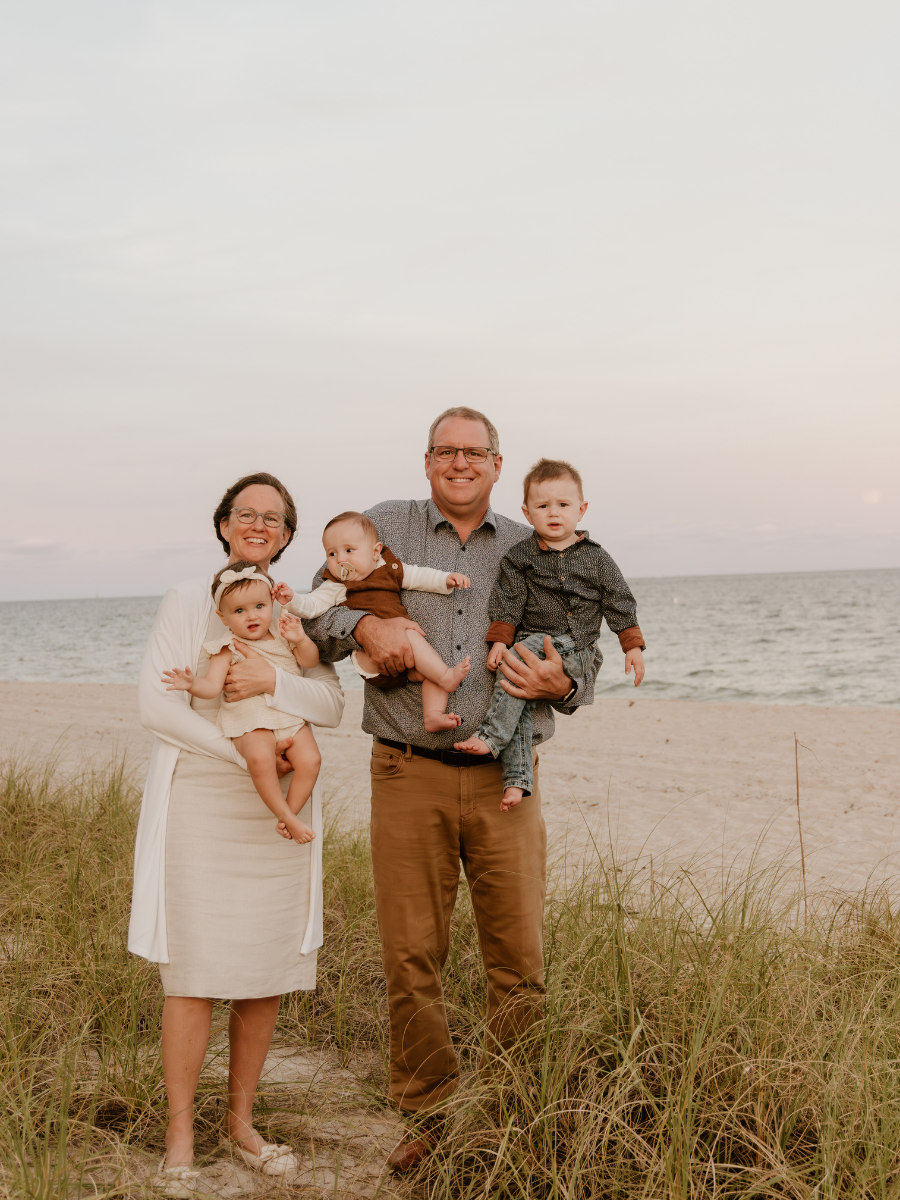 Family of five standing on the beach with the ocean and sky in the background, smiling and posing for a photo.