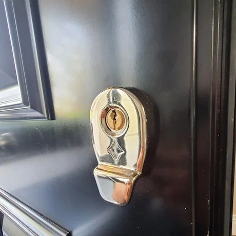 Close-up of a door lock mechanism on a black door with a portion of a window visible.