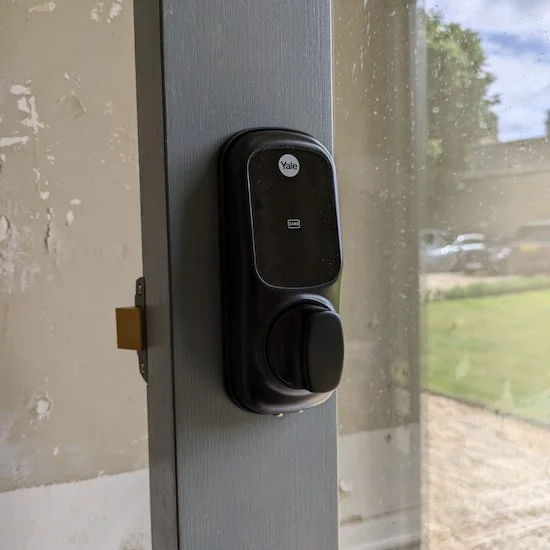 Black Yale electronic door lock mounted on a gray door frame, with a partial view of an outside area with cars and trees through the glass window.