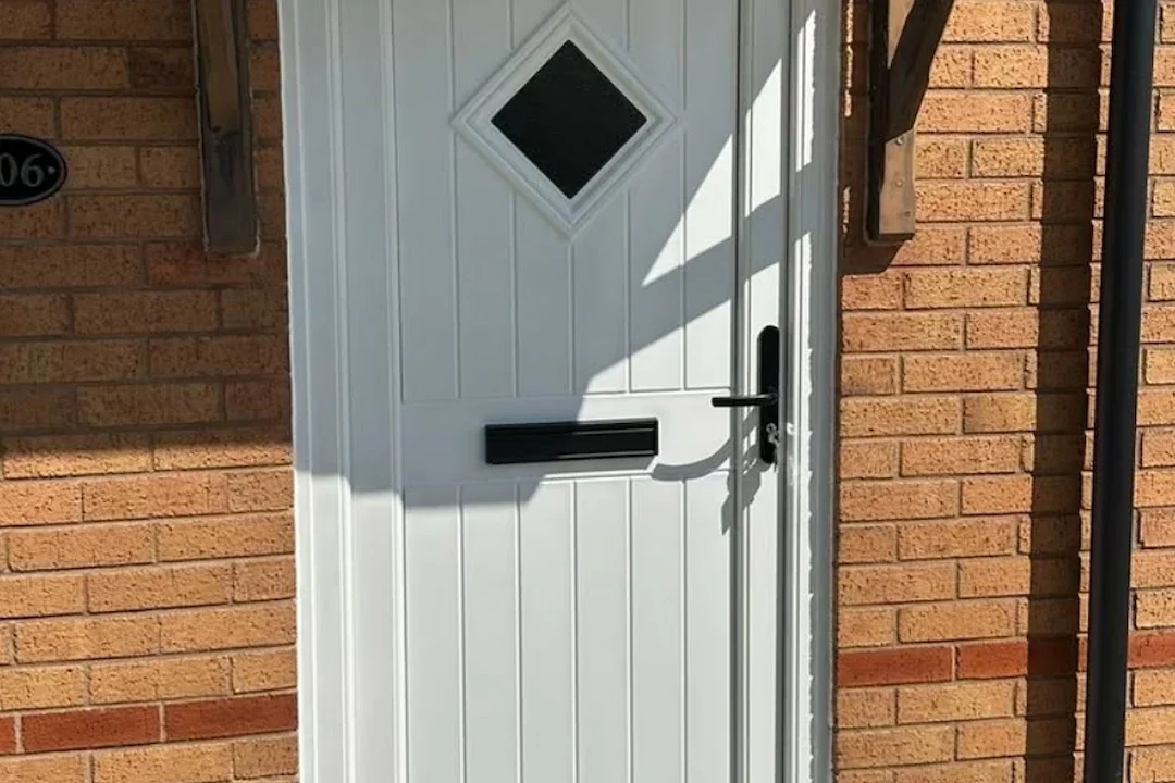 White uPVC front door with diamond-shaped window and mail slot, set in a brick wall with black house number plaque.