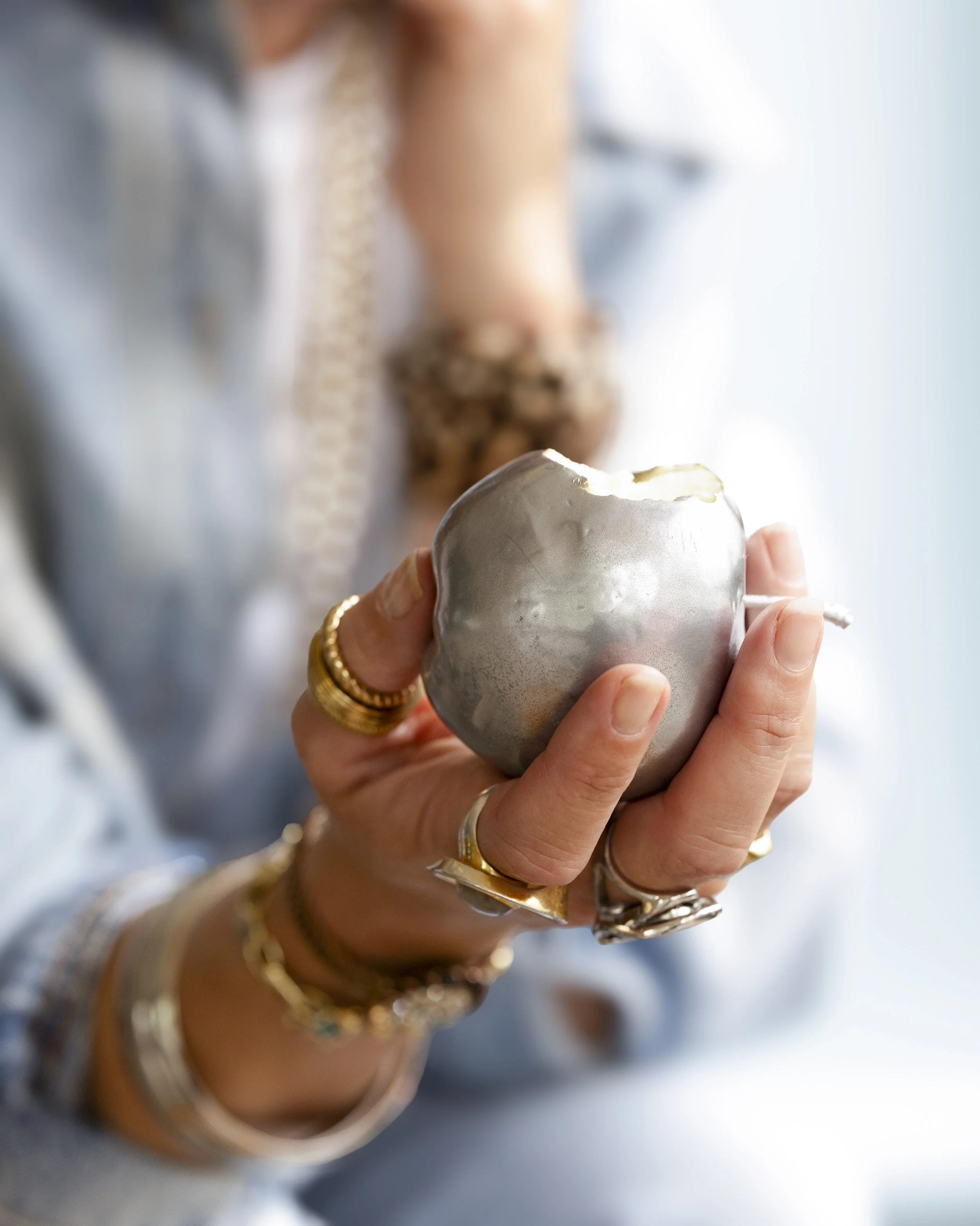 Person holding a silver cup with white frosting on top, wearing gold rings and bracelets.