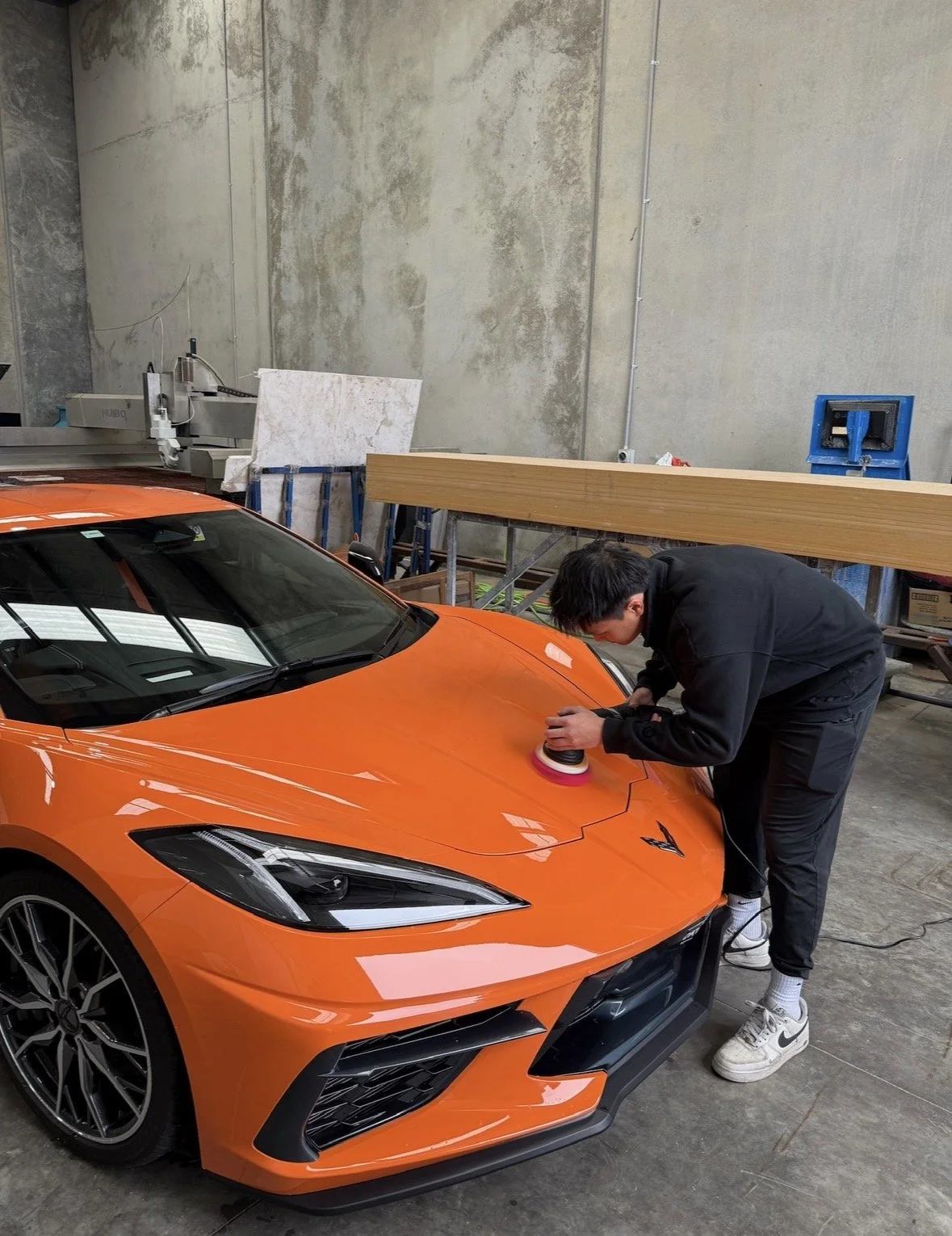 A person polishing the hood of an orange sports car inside a workshop.
