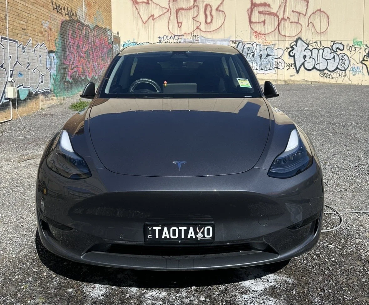 Black Tesla Model 3 parked in front of a graffitied wall.