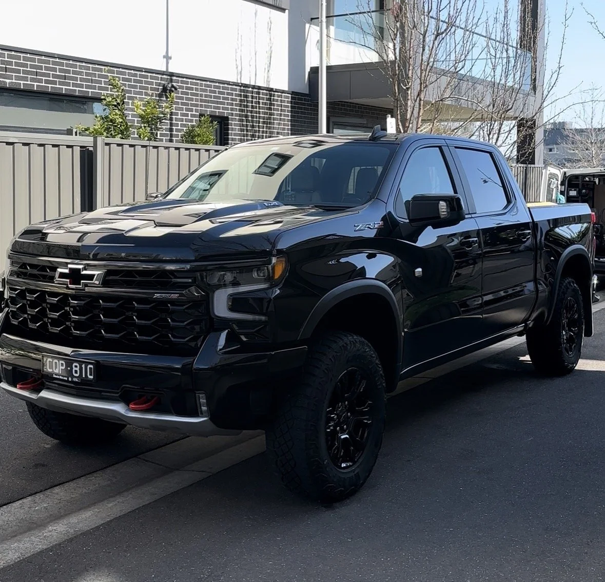 Black Chevrolet Silverado pickup truck parked on the street in front of a modern residential building.