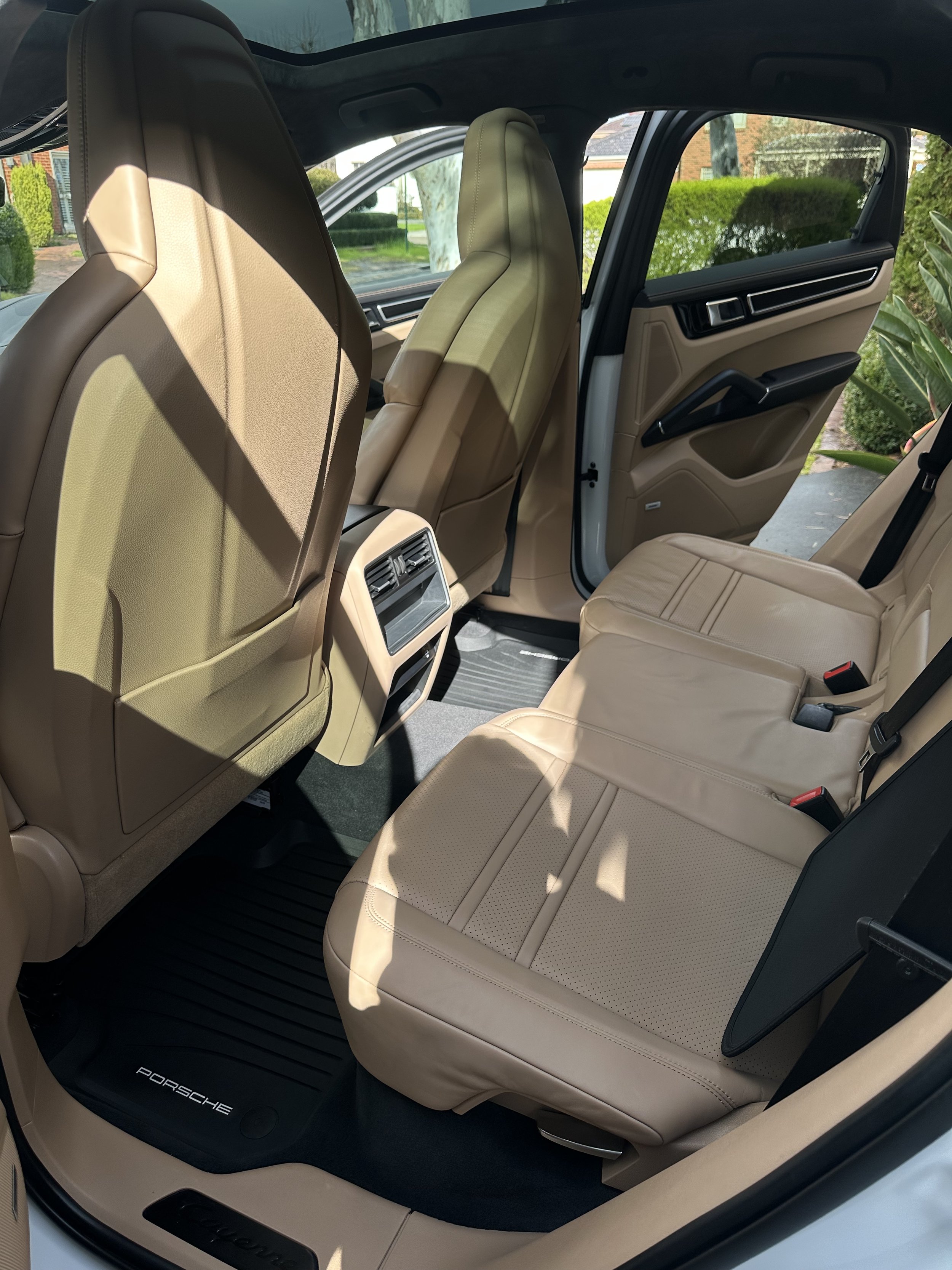 The interior of a luxury car with beige leather seats and black accents, showing the back seat area, front seats, and the side door with window.