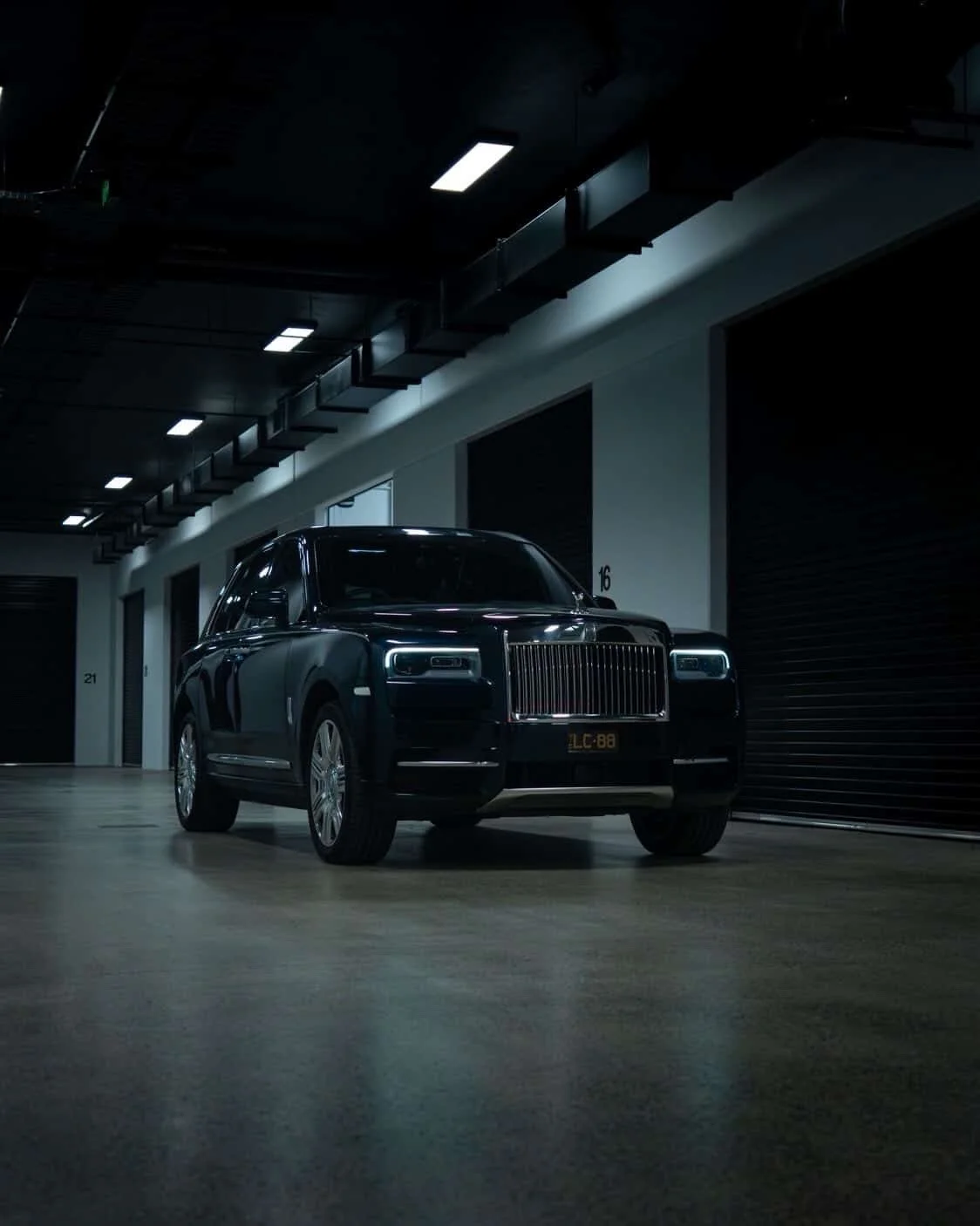 A black luxury SUV parked inside a dimly lit garage with black painted roll-up doors and numbered labels.