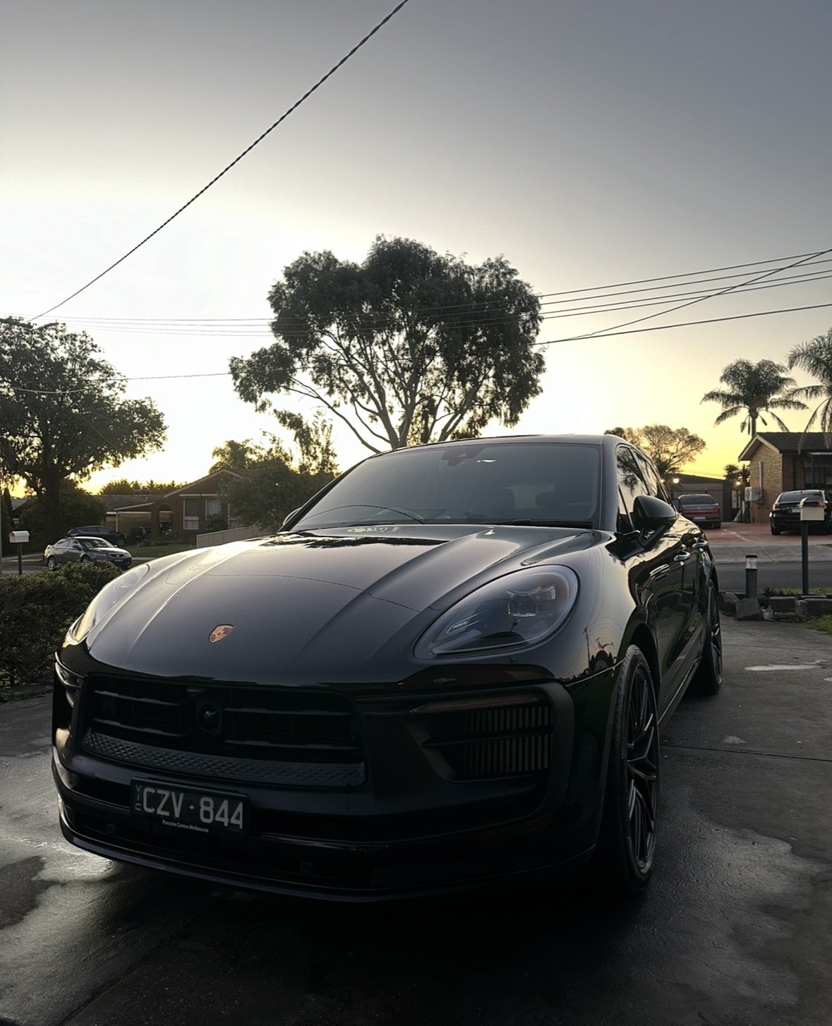 Black Porsche Macan parked outdoors during sunset with trees and houses in the background.