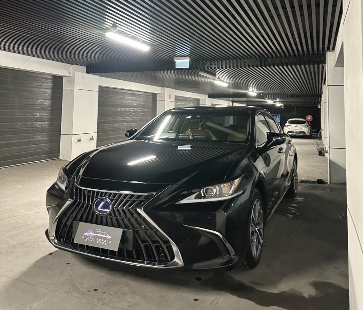 A black Lexus sedan parked inside a well-lit underground garage with closed gray doors on the side.
