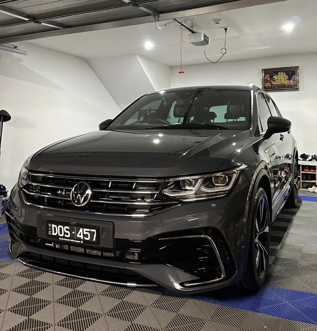 Black Volkswagen SUV parked inside a garage, with a white wall and overhead equipment visible.